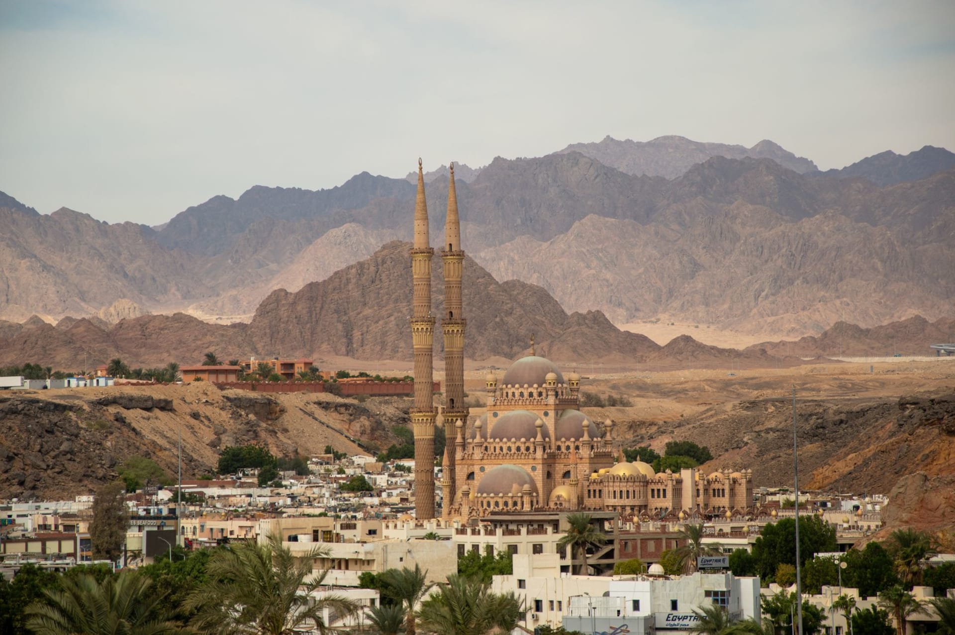 A turquoise bay framed by desert mountains at Sharm el-Sheikh's Naama Bay, with a wooden pier extending into glassy water at golden hour