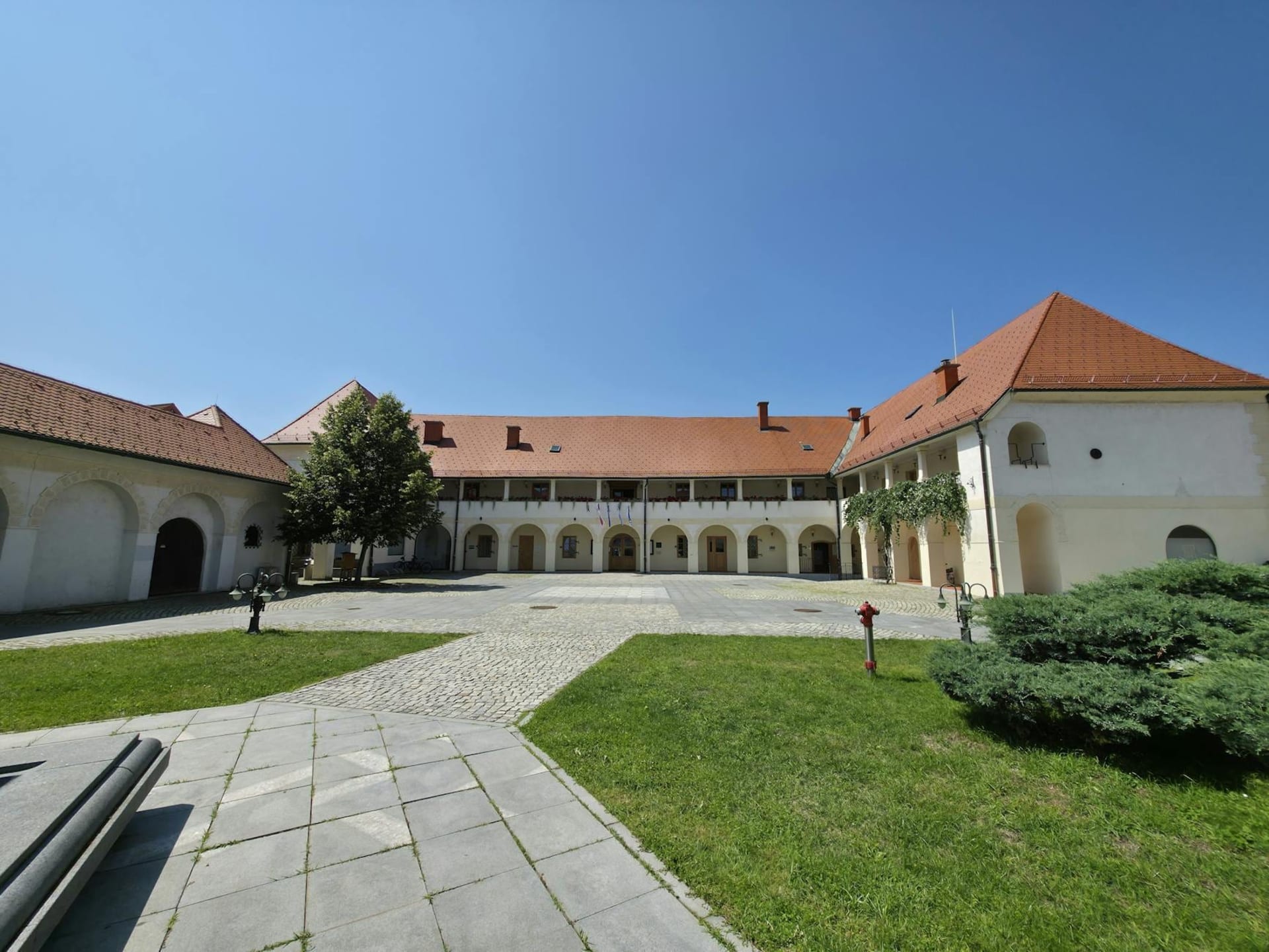 The Old Vine House along the Drava riverfront in Maribor, its stone facade draped with ancient grapevine tendrils, warm afternoon light on the water and Lent quarter promenade below