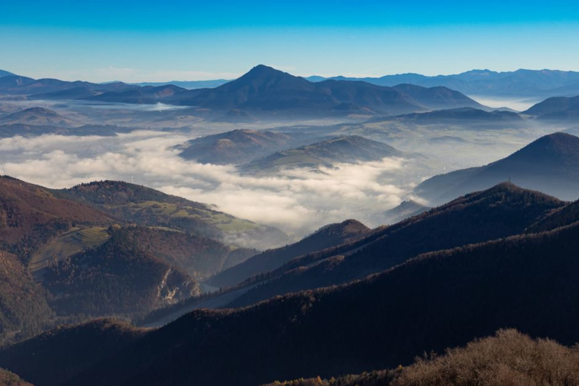 Rows of vines climbing terraced hillsides in the Vipava Valley with a stone village and the Nanos plateau rising in the background under a clear sky