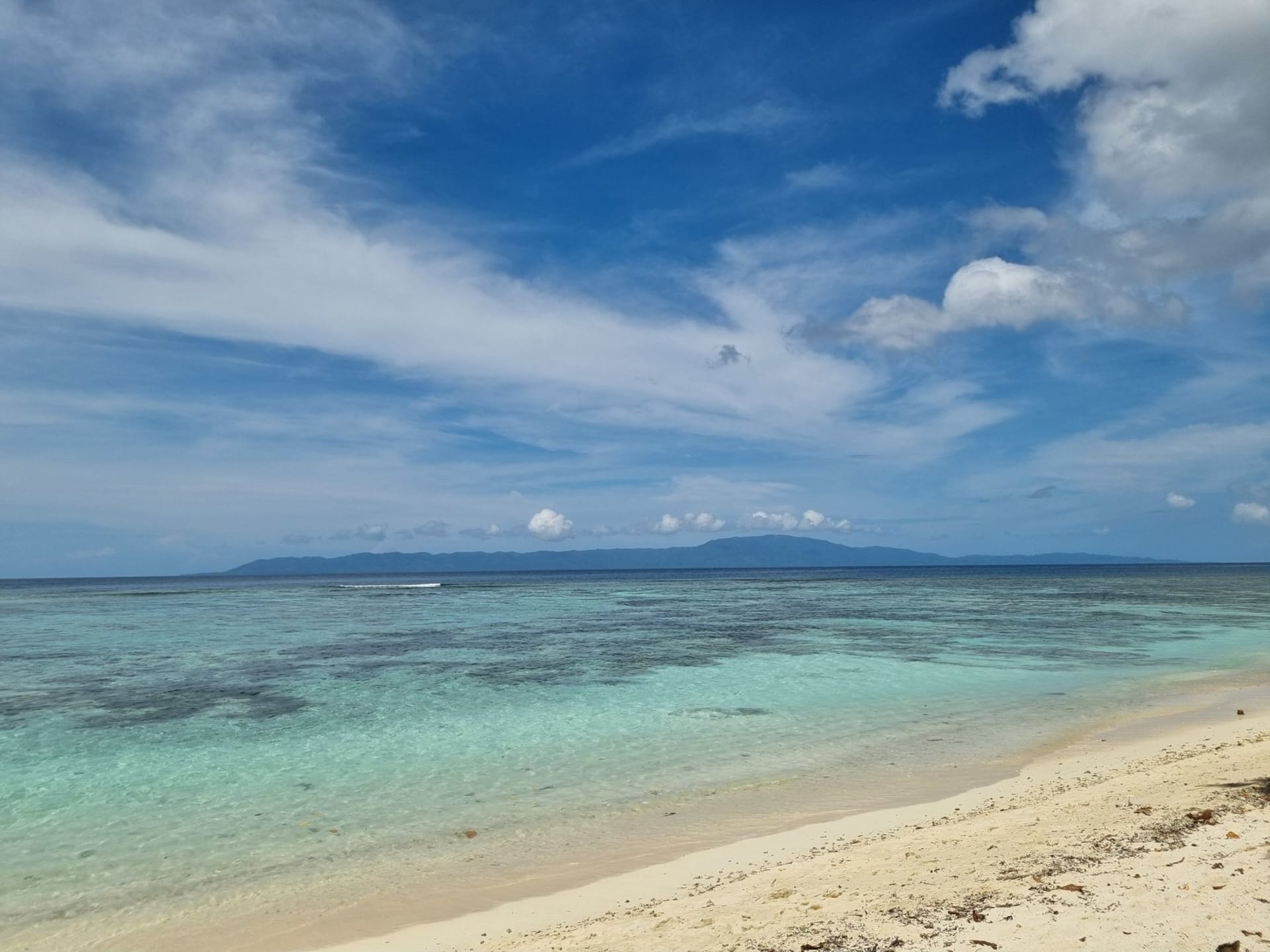 The tranquil beach of Gizo, Solomon Islands, with flat clear turquoise water and a white sandy shore backed by dense tropical vegetation