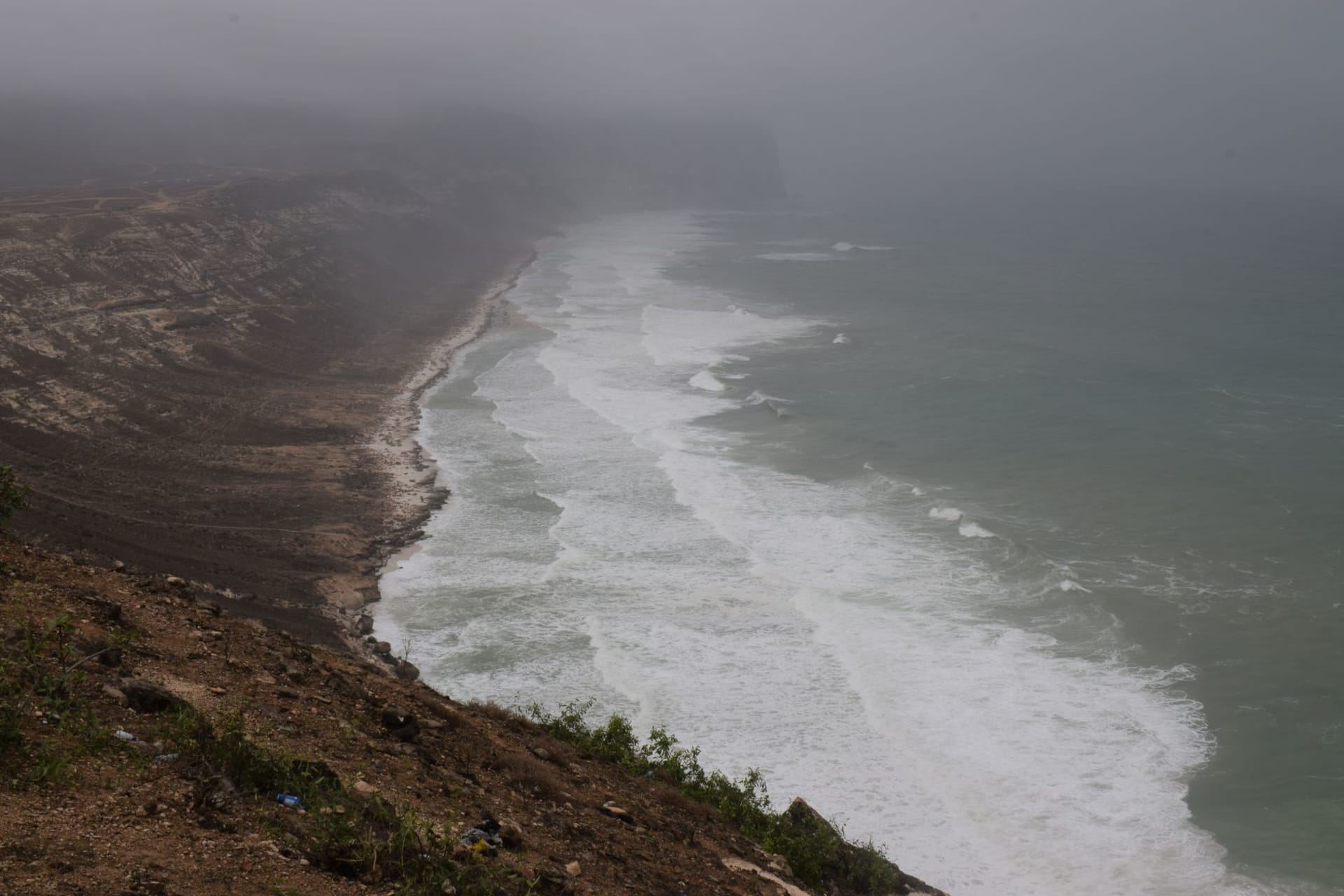 Playa de coral virgen en la costa de Puntlandia al amanecer con árboles de incienso en la ladera rocosa de arriba, agua turquesa y un dhow de pesca solitario anclado frente a la orilla