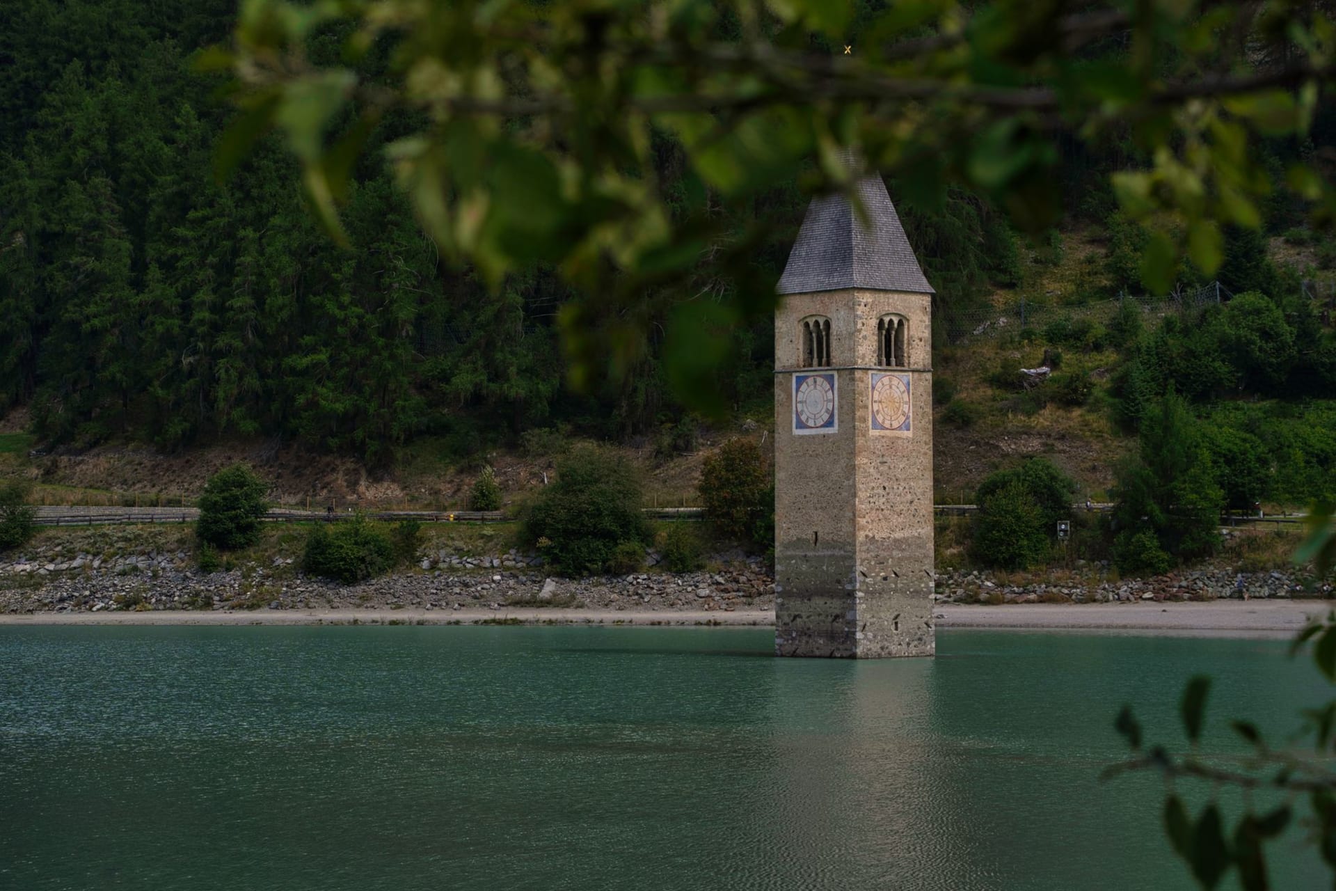 Le clocher médiéval du village submergé de Graun s'élevant de la surface grise et immobile du Reschensee en hiver, entouré d'eau gelée et encadré par les sommets enneigés de l'Ortles