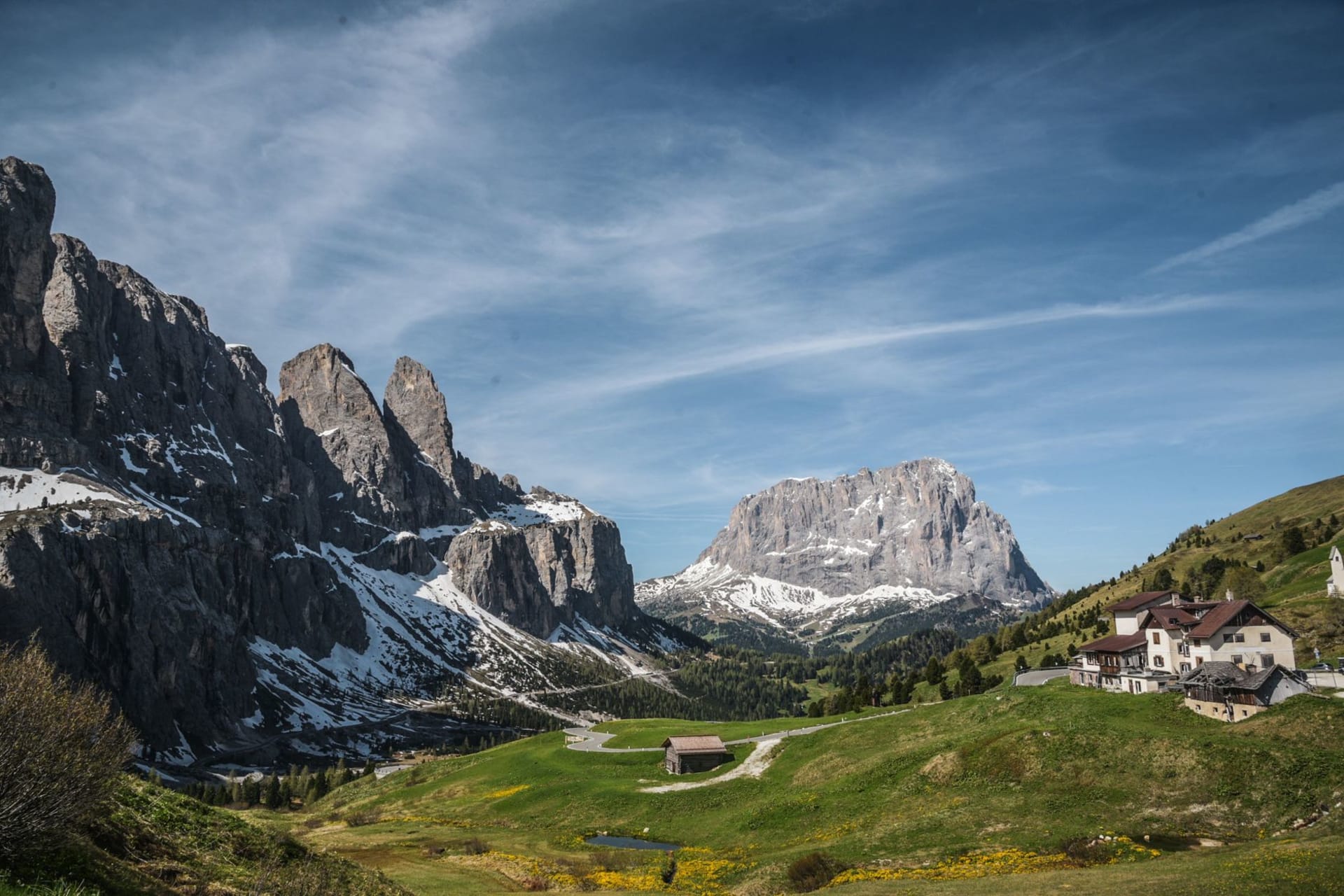 The village of Ortisei in Val Gardena with painted wooden chalets and a baroque church spire, backed by the sheer grey walls of the Sassolungo massif in late afternoon light