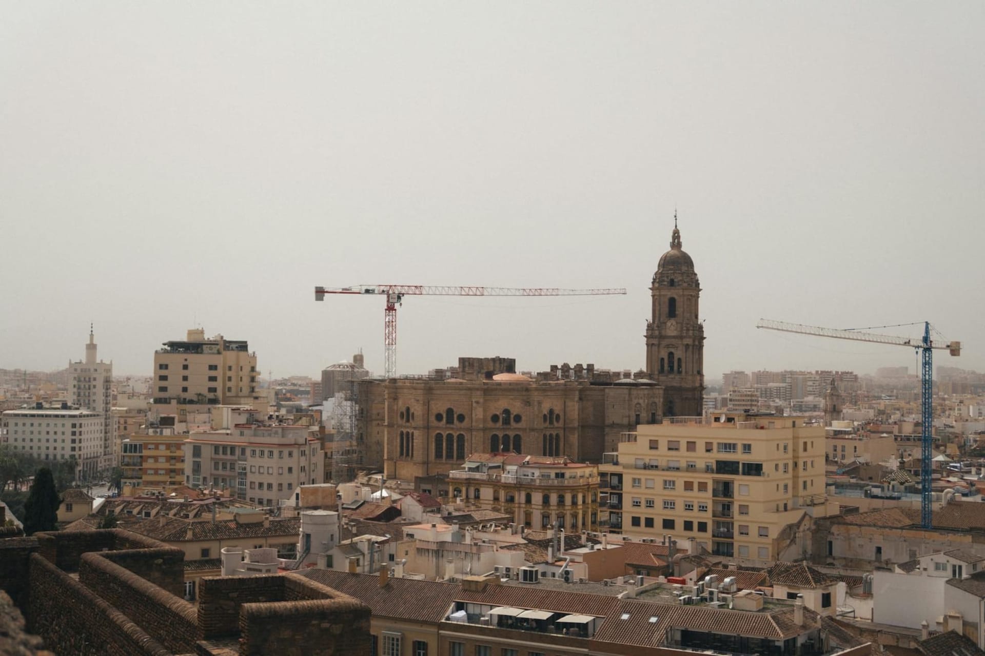 The Alcazaba fortress rising above sun-bleached rooftops in central Malaga, with the cathedral dome and the shimmering Mediterranean visible in the distance