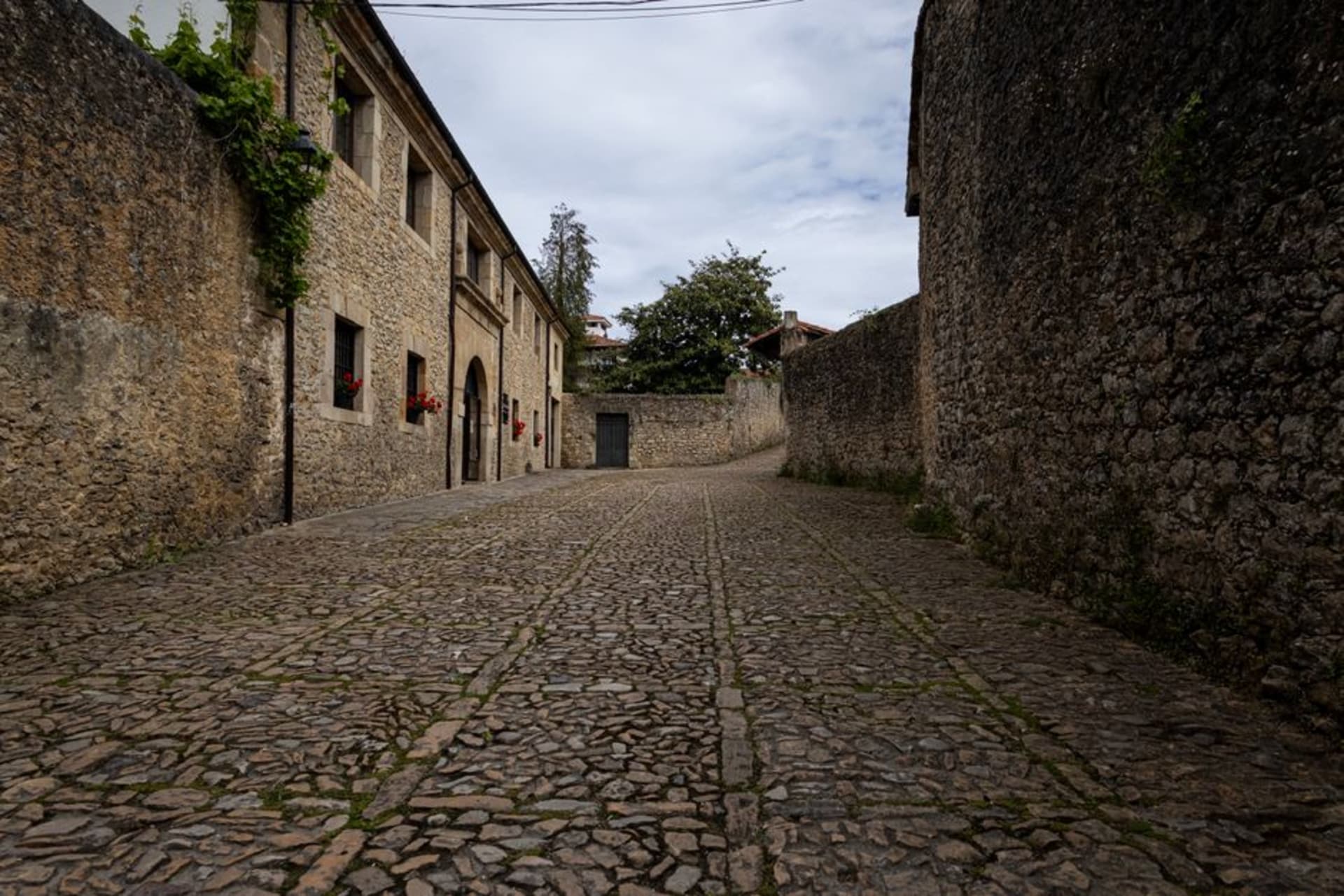 Cobbled main street of Santillana del Mar lined with medieval stone manor houses and wooden balconies under a grey Cantabrian sky