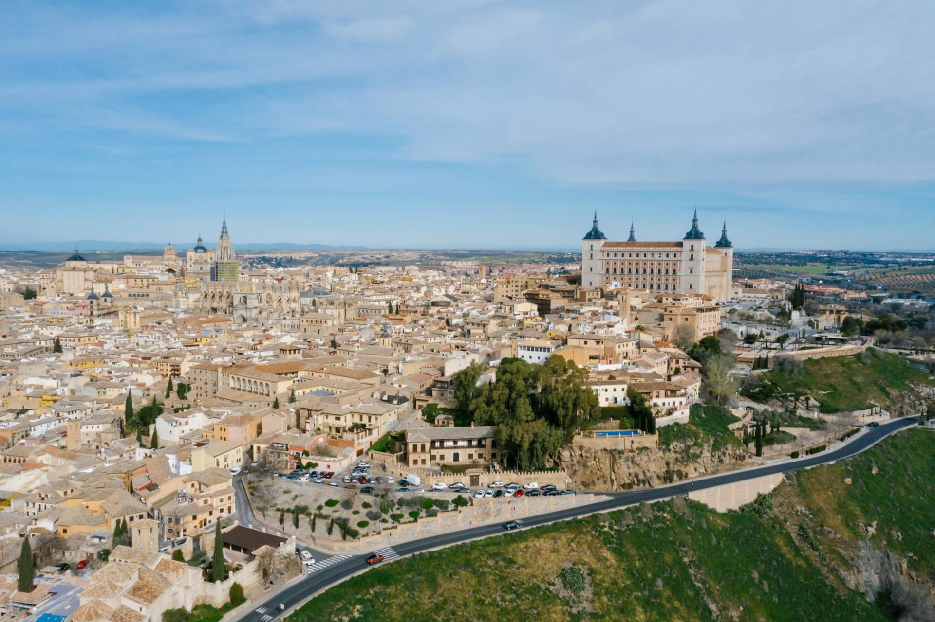 Toledo's medieval skyline rising above the Tagus river gorge at dusk, the Alcázar fortress and cathedral tower lit gold against a bruised violet sky