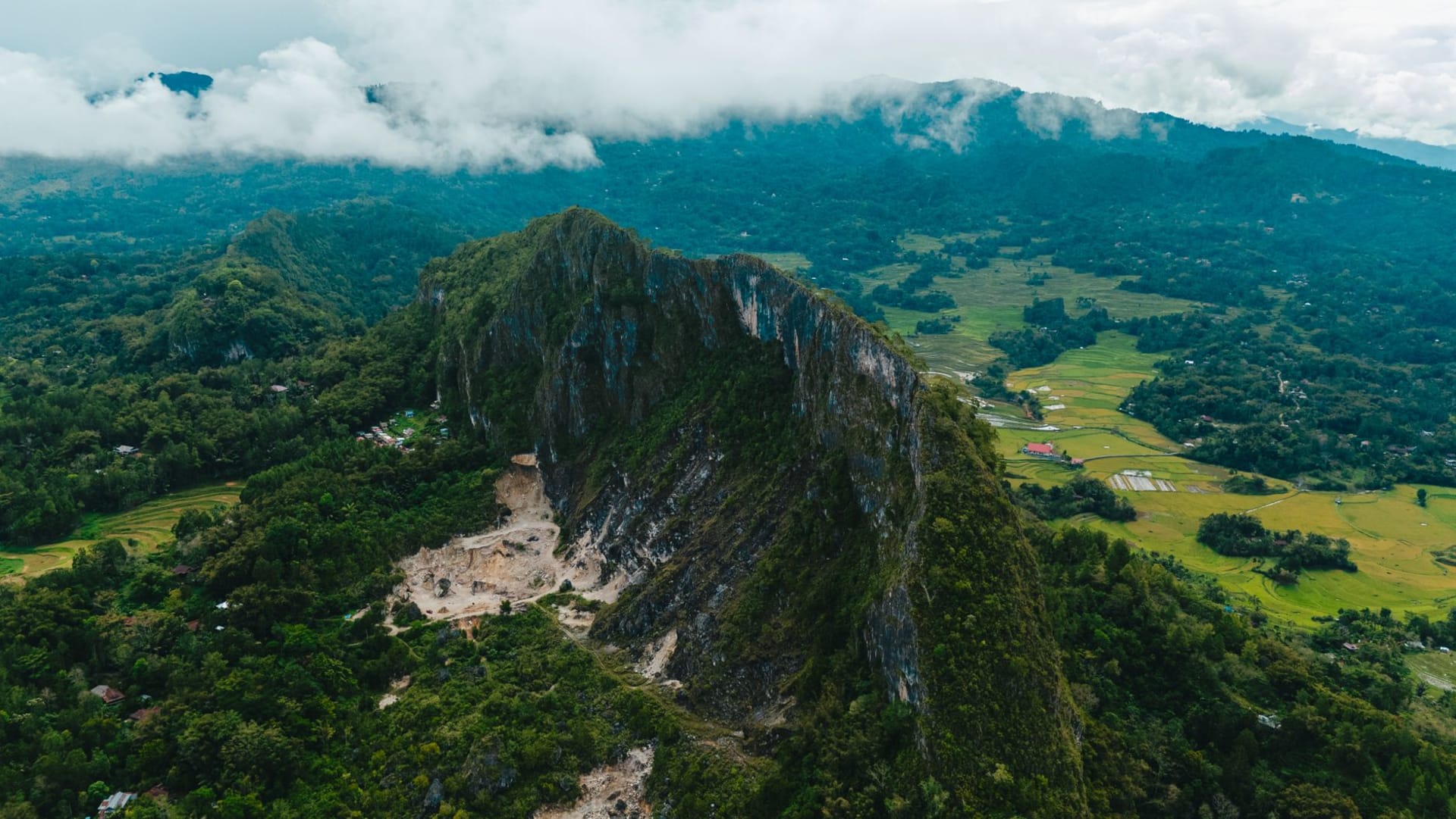 El cono volcánico del Monte Lokon elevándose sobre la ciudad de Tomohon en las tierras altas de Minahasa, con árboles de clavo y niebla en primer plano