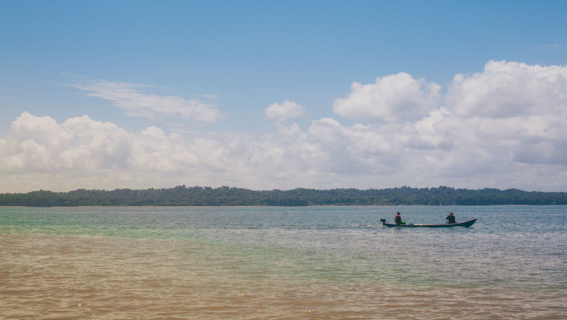 Des troncs d'arbres morts et blanchis émergeant de la surface sombre et immobile du réservoir de Brokopondo à l'heure dorée, avec une jungle ininterrompue sur la rive lointaine et un étroit canoë en bois au premier plan
