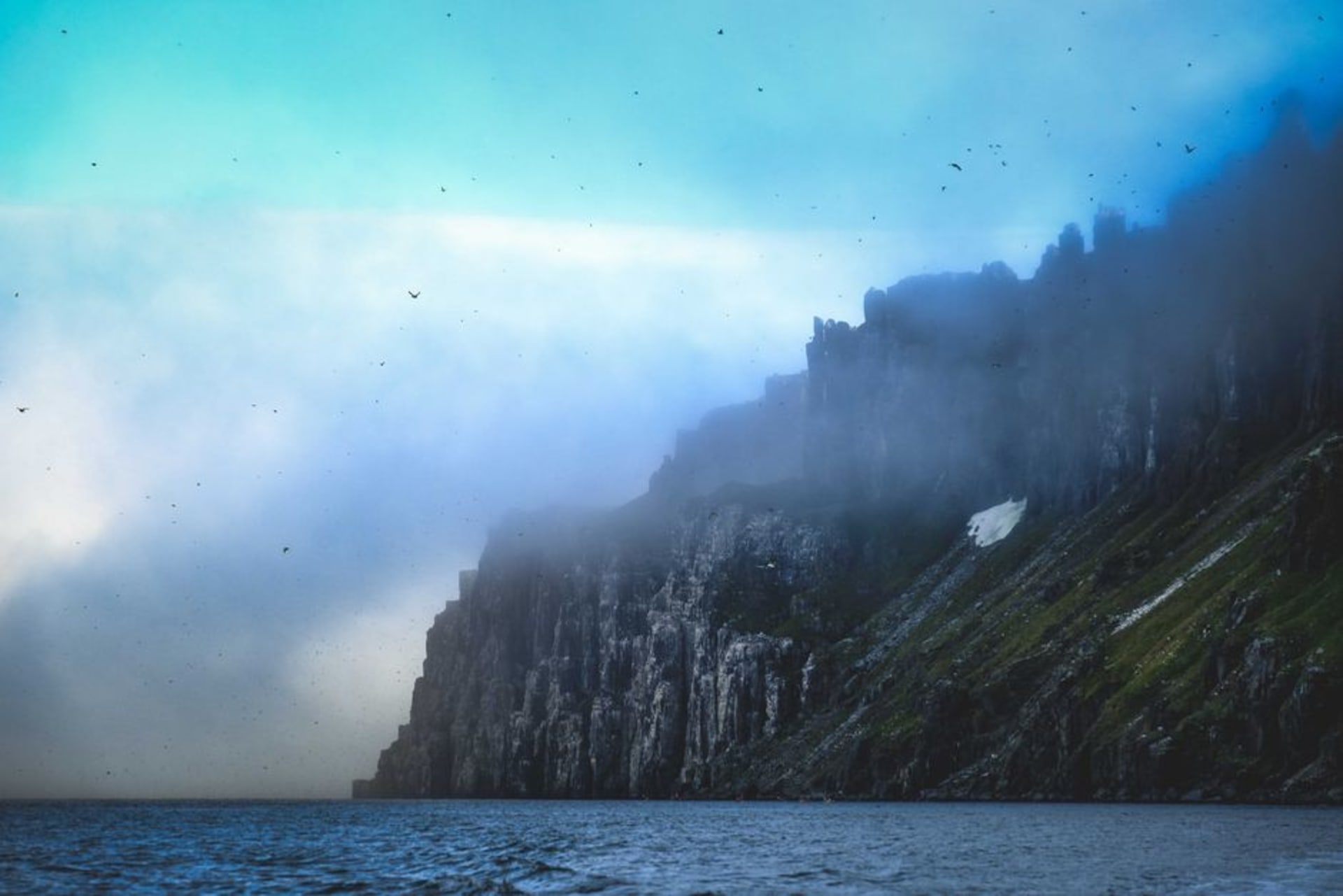 Steep dark cliffs of Bear Island rising out of the misty Barents Sea