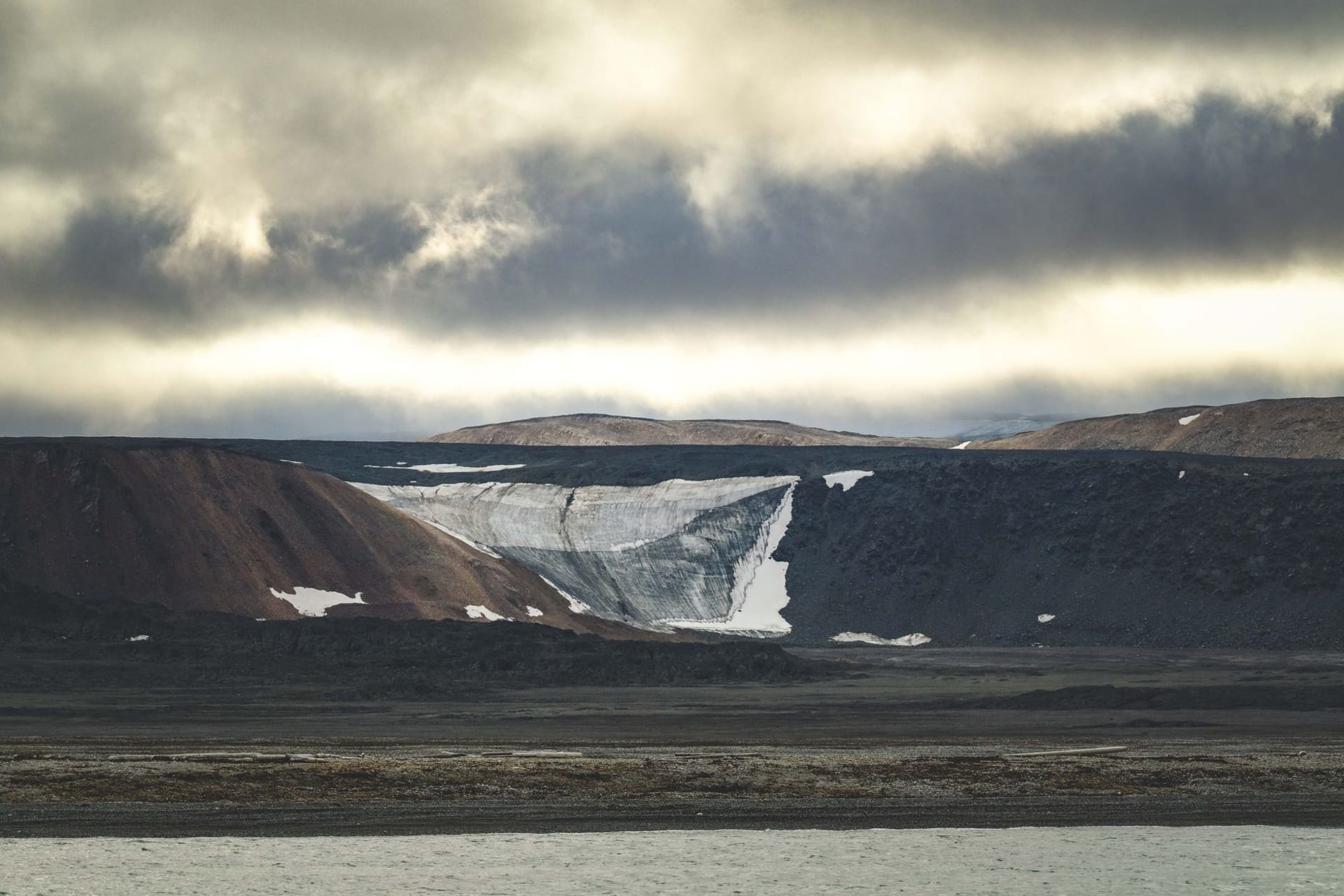 Soviet-era apartment buildings and a prominent Lenin mural painted on a concrete wall overlooking a grey Arctic fjord, coal-stained buildings in the foreground
