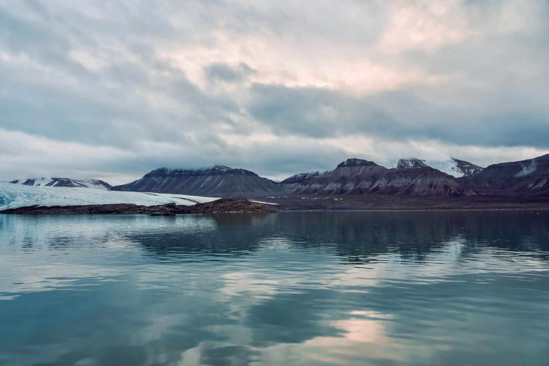 A flat Arctic tundra landscape with braided river channels in the foreground, a walrus haul-out visible on a gravel spit, and the open Barents Sea in the distance under heavy cloud