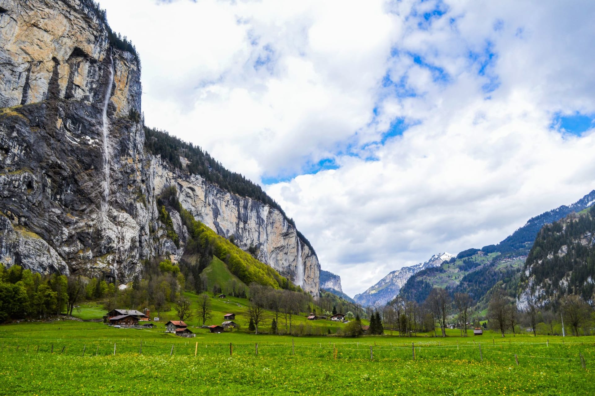 The Lauterbrunnen valley floor with the Staubbachfall waterfall dropping nearly 300 meters down a sheer limestone cliff face, the valley walls enclosing a narrow strip of green and sky