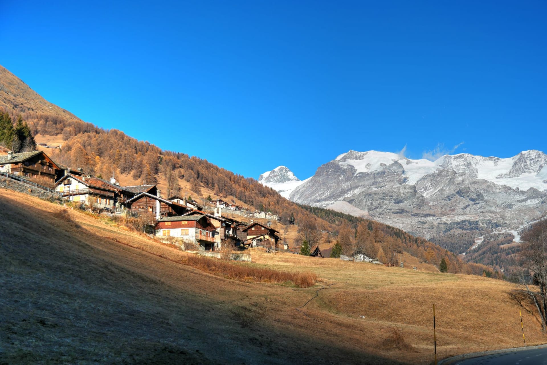 Saas-Fee village of dark timber chalets clustered beneath the Fee Glacier, the ice tongue descending visibly between two rock ridges in afternoon shadow