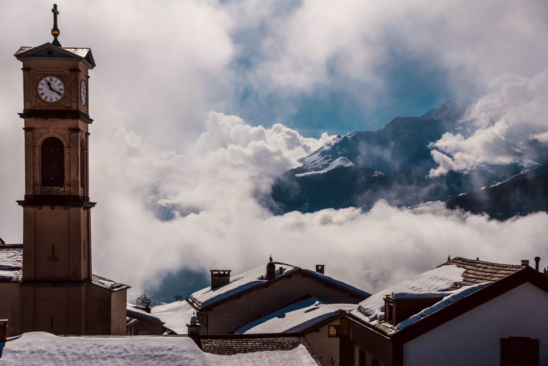 Wide view of Verbier's wooden chalets and modern apartment blocks spread across a south-facing alpine shelf, with the Grand Combin massif dominating the horizon under winter sun