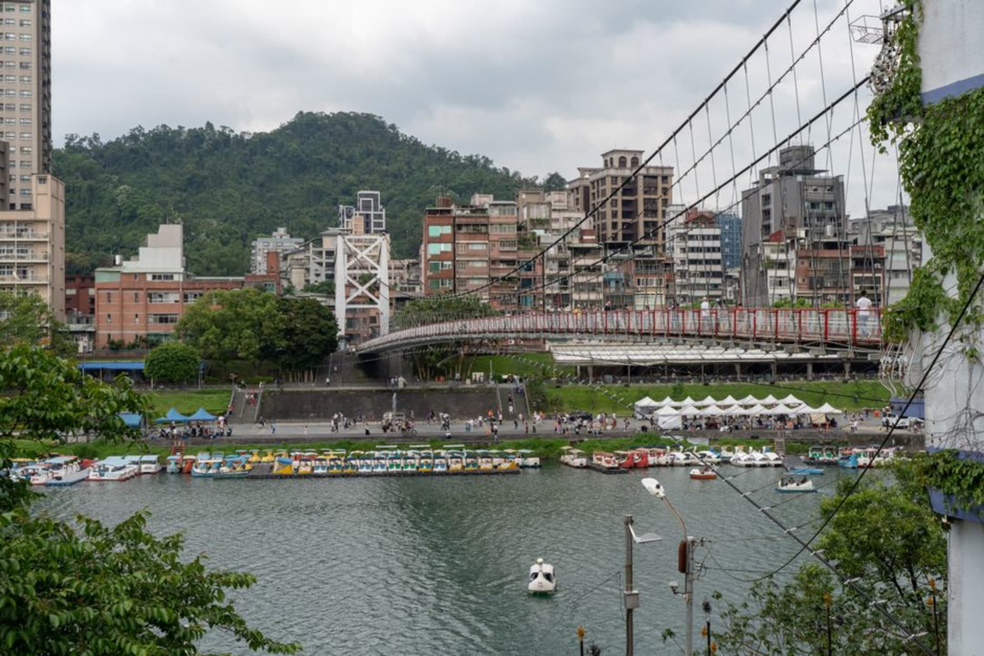 The red suspension bridge over the jade-green waters of Bitan reservoir, paddle boats scattered across the surface below
