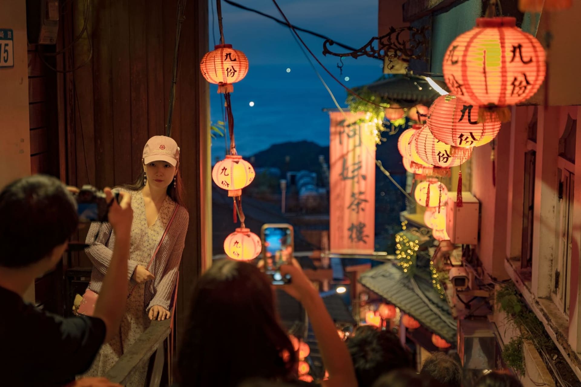 Red paper lanterns glowing amber above the narrow stone steps of Jiufen Old Street, with wooden teahouses jutting out over a fog-wrapped hillside and the dark Pacific below