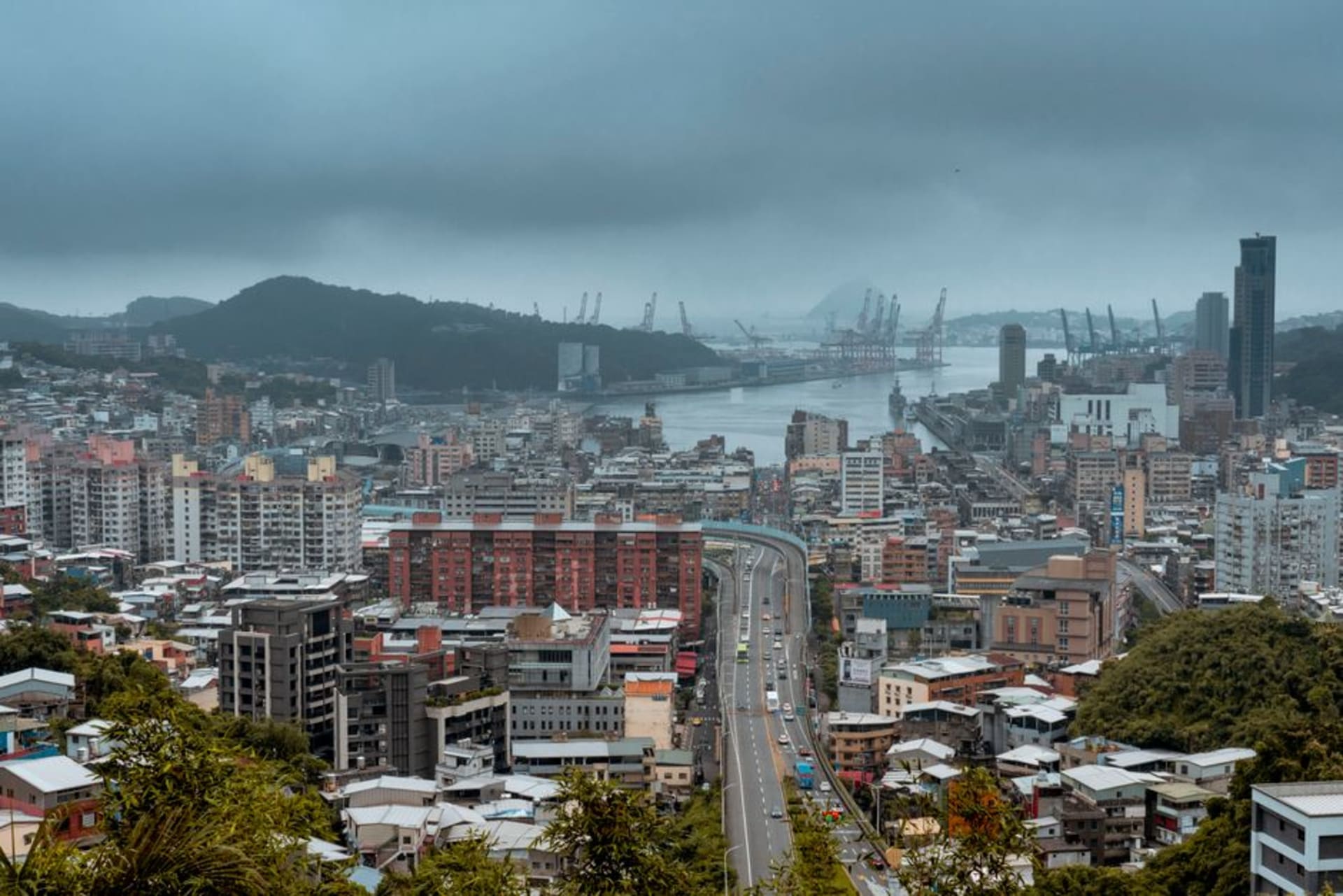 Des porte-conteneurs et des bateaux de pêche dans le port de Keelung au crépuscule, avec la ville en pente qui s'élève derrière le port