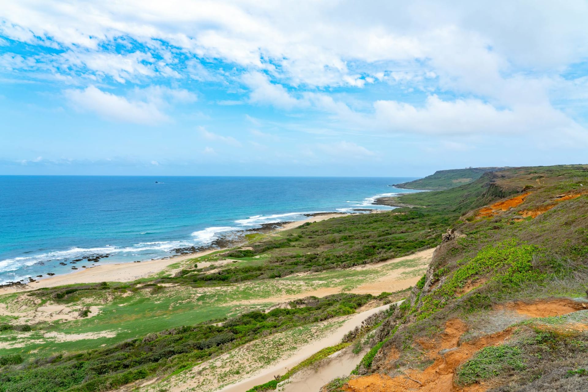Turquoise water lapping against a white coral-sand beach in Kenting National Park, with dense green headlands dropping into the sea under a cloudless southern Taiwan sky.