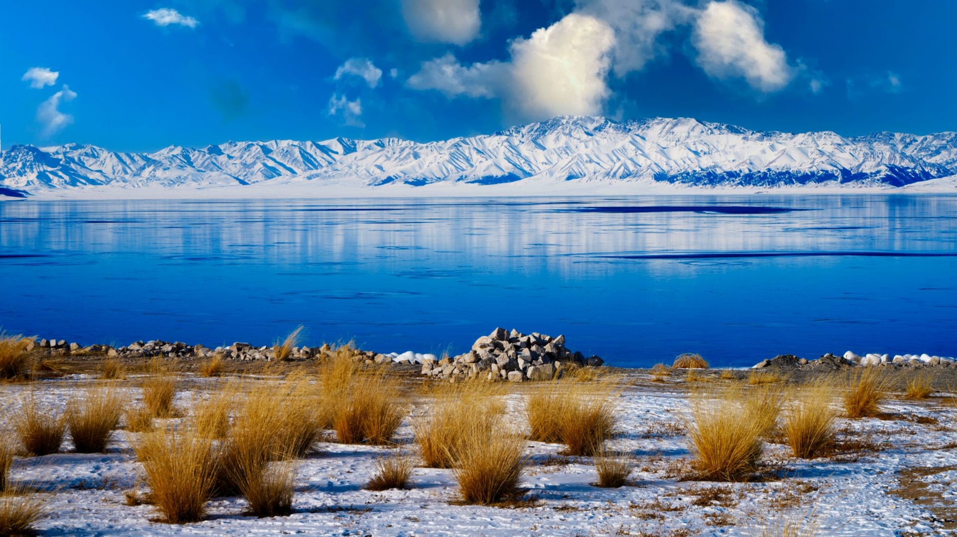 The deep blue expanse of Karakul Lake on the high Pamir plateau in Tajikistan, snow-capped peaks ringing the far shore under a vast pale sky
