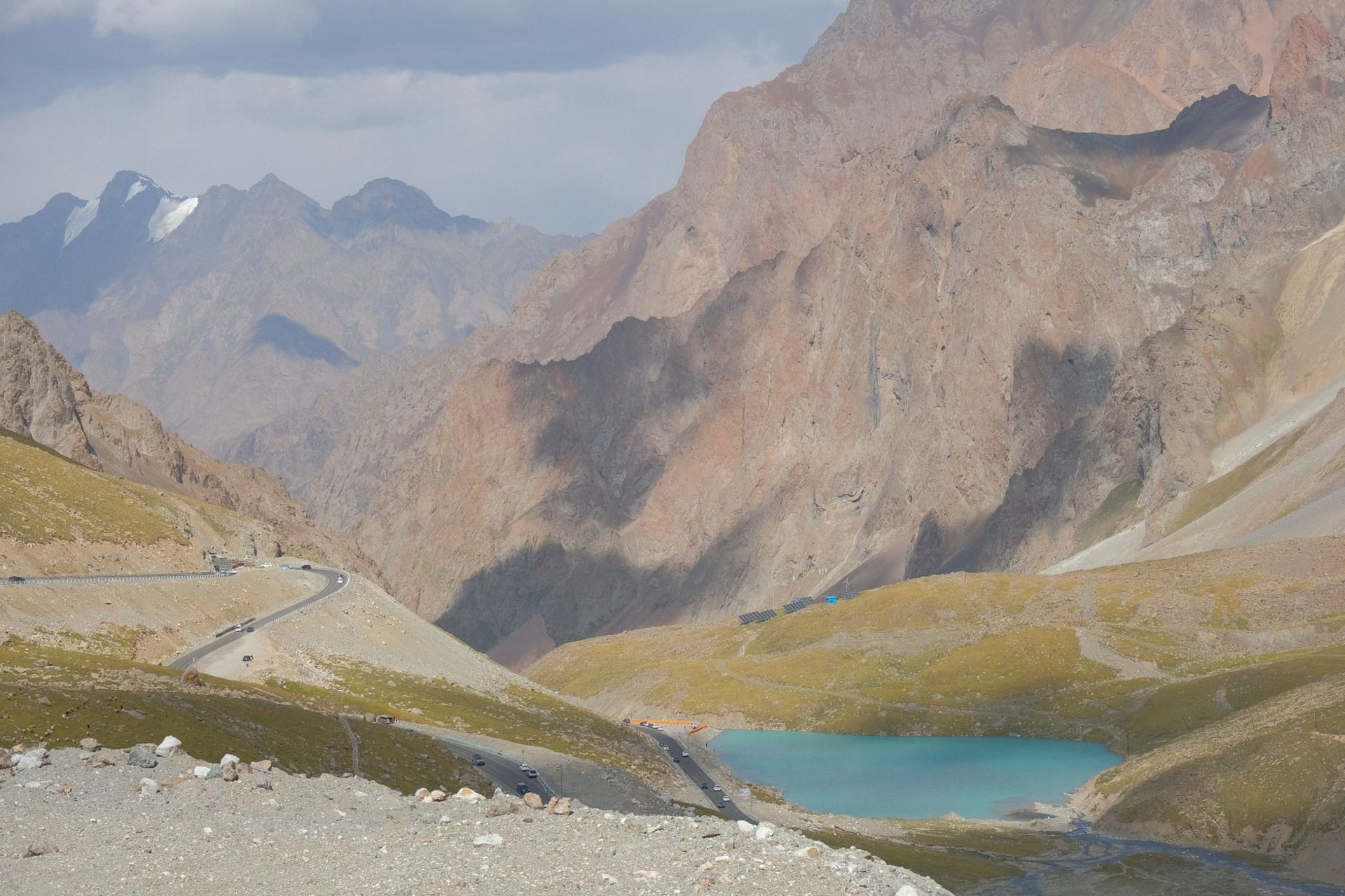Turquoise lake surface reflecting jagged snow-streaked limestone peaks, with a lone pine on a rocky shoreline in the foreground