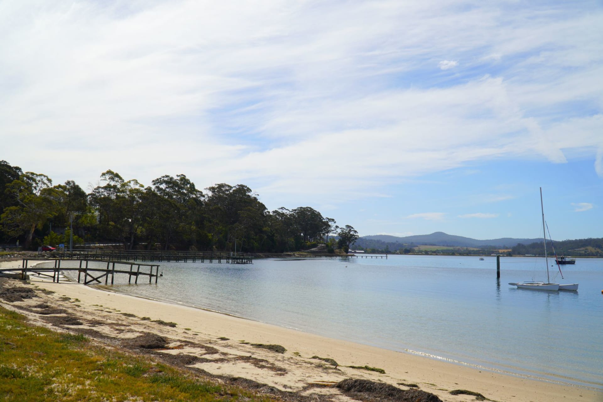 The narrow sand isthmus connecting North and South Bruny Island at low tide, with dark water on both sides and a lighthouse visible on the distant headland