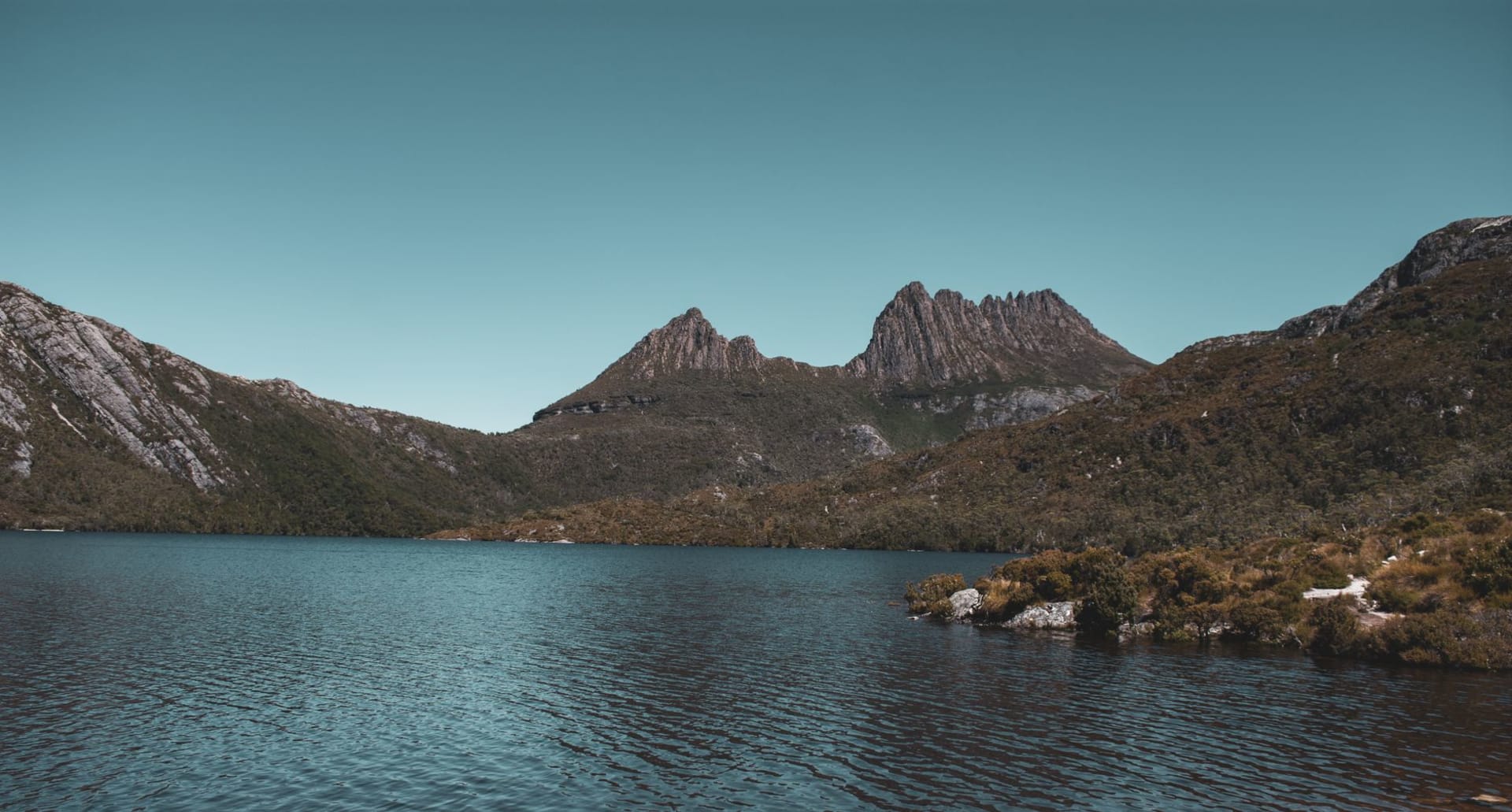 Cradle Mountain's jagged twin peaks reflected perfectly in the still surface of Dove Lake at dawn, surrounded by ancient pencil pine forest