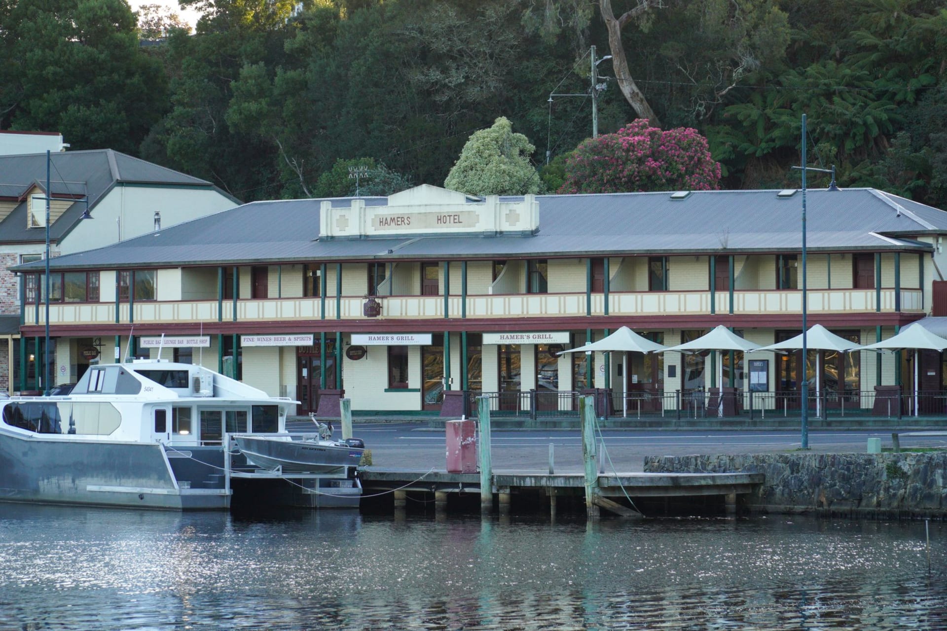 A wooden cruise boat moving through the mirror-still tannin-dark waters of the Gordon River, surrounded by ancient Huon pine forest under an overcast Tasmanian sky
