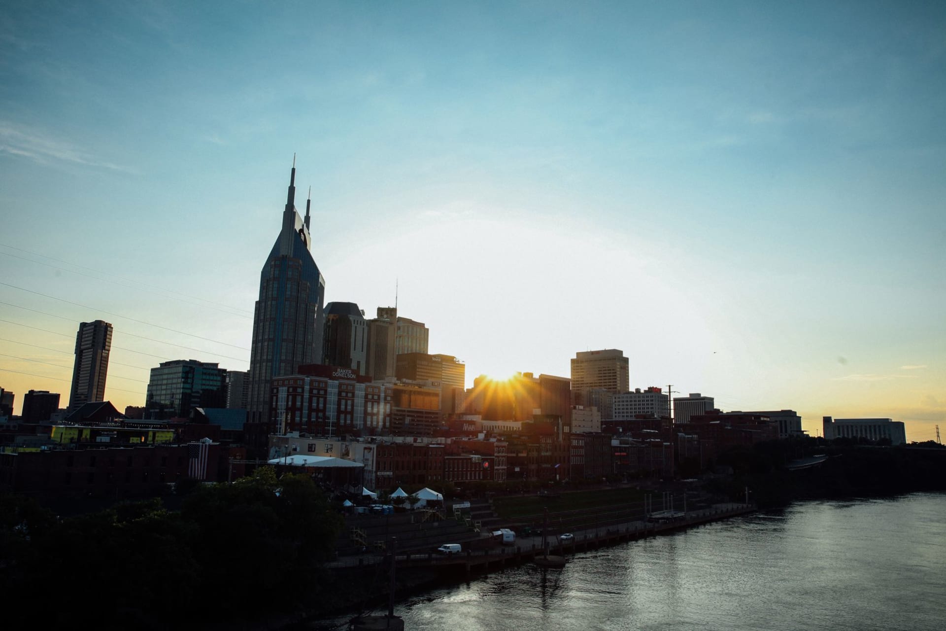 Nashville skyline at sunset reflected in the calm waters of the Cumberland River, warm orange light washing over downtown towers