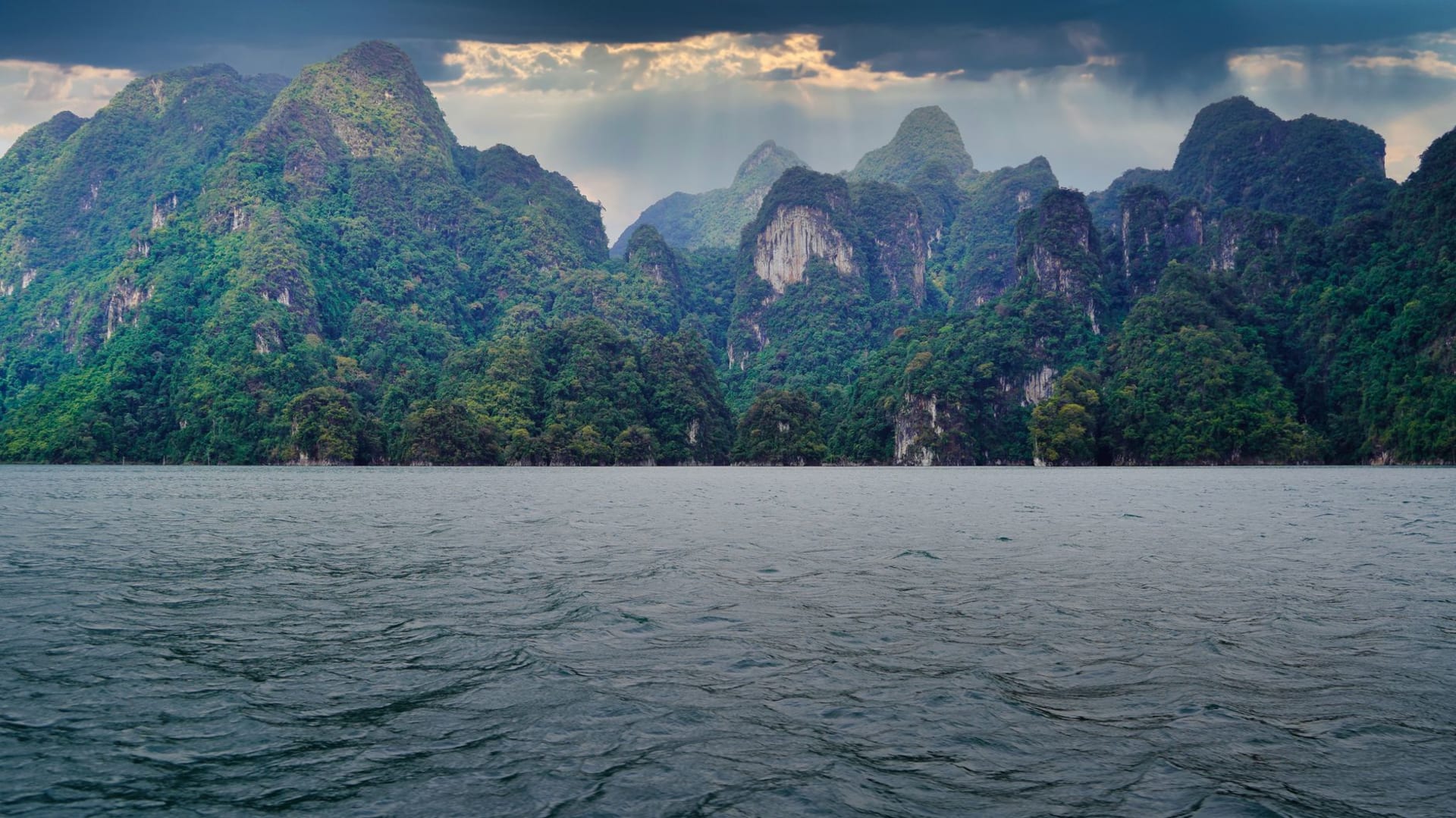 Towering limestone karsts draped in jungle rising from the still emerald water of Cheow Lan Lake in Khao Sok at dawn