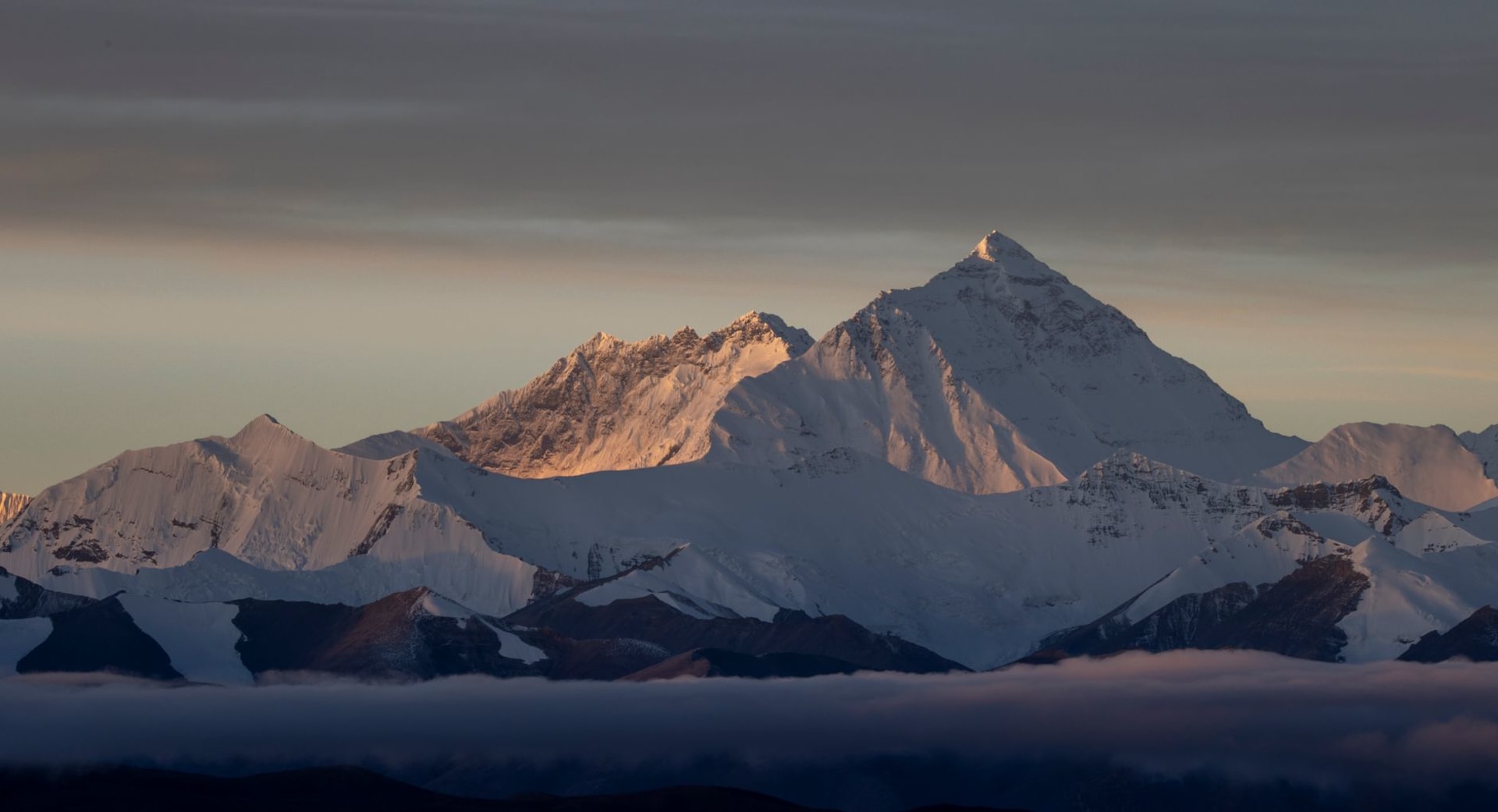 Mount Everest's north face rising above the Rongbuk Glacier under a clear blue sky at dawn, with prayer flags in the foreground