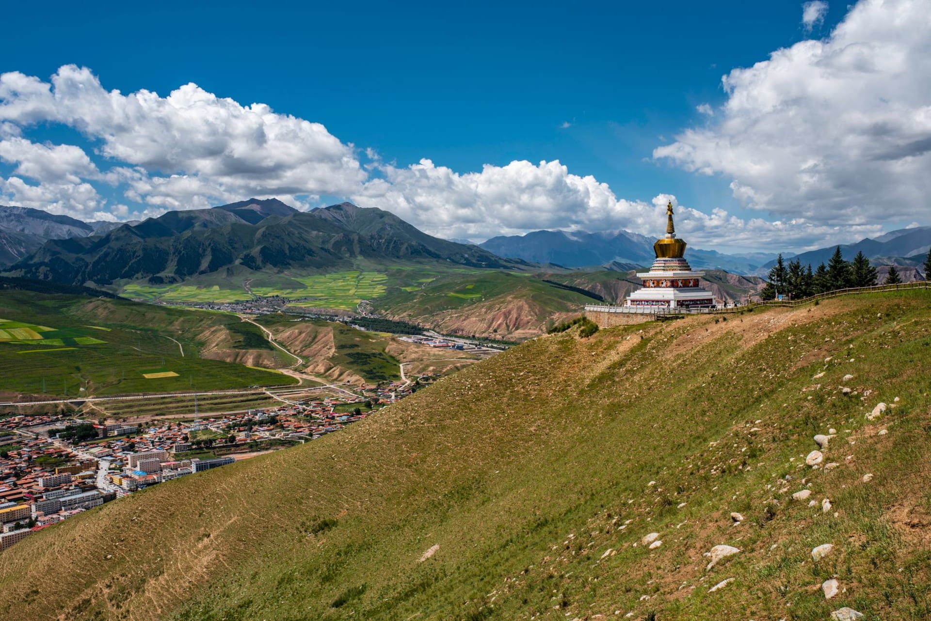 The green Yarlung Valley floor with barley fields and traditional Tibetan farmhouses, framed by dry brown hillsides under a clear sky