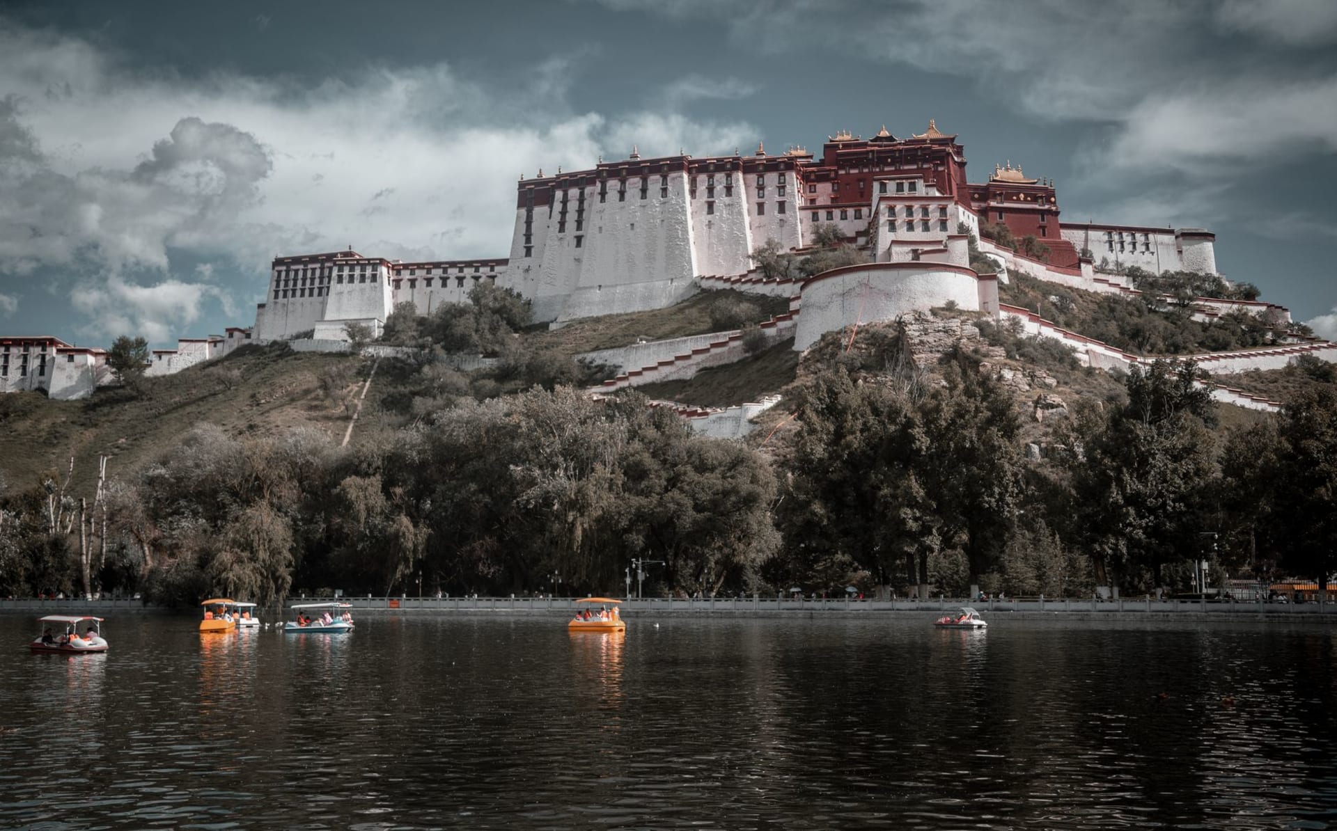 The Potala Palace rising above a calm reflective lake in Lhasa, Tibet, under a vast open sky