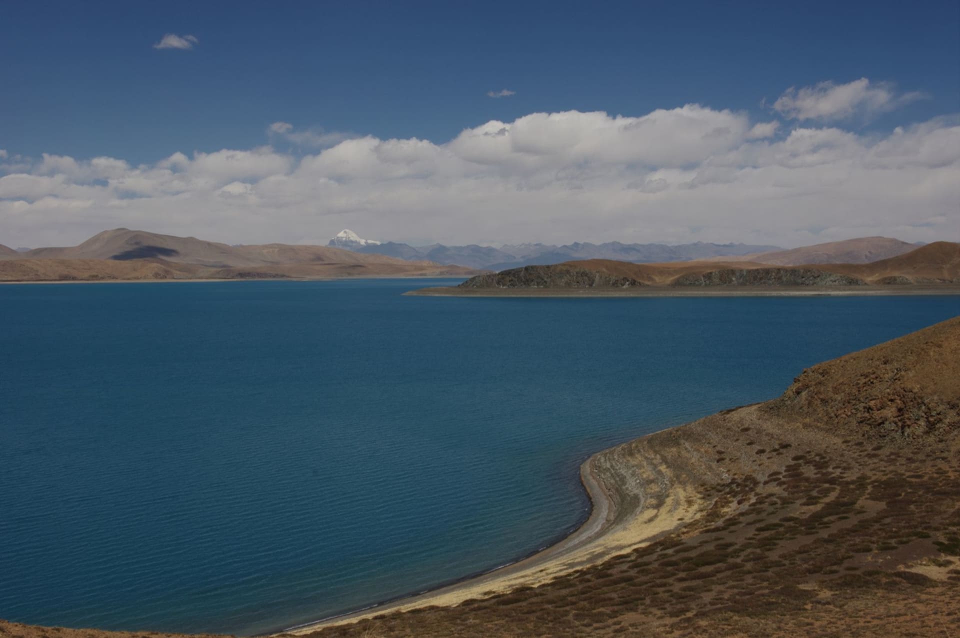 The intensely turquoise waters of Yamdrok Lake winding between bare brown mountains under a deep blue Tibetan sky