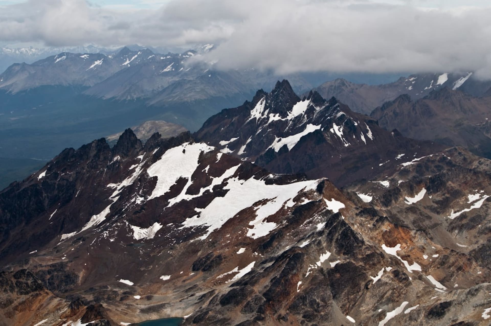 Looking down over Ushuaia's harbor and the Beagle Channel from the rocky trail near Martial Glacier, with snowfields visible above and the town spread across the hillside below