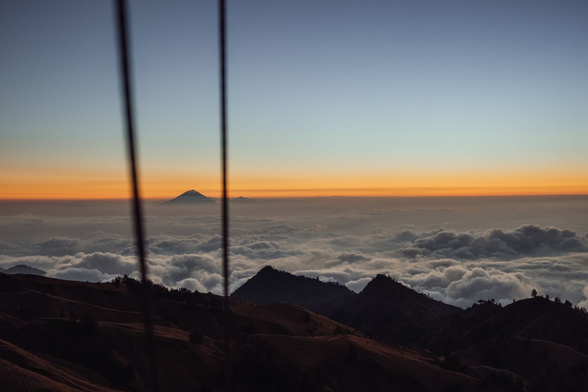 A white statue of the Virgin Mary on the summit of Mount Ramelau silhouetted against a glowing dawn sky above a sea of cloud