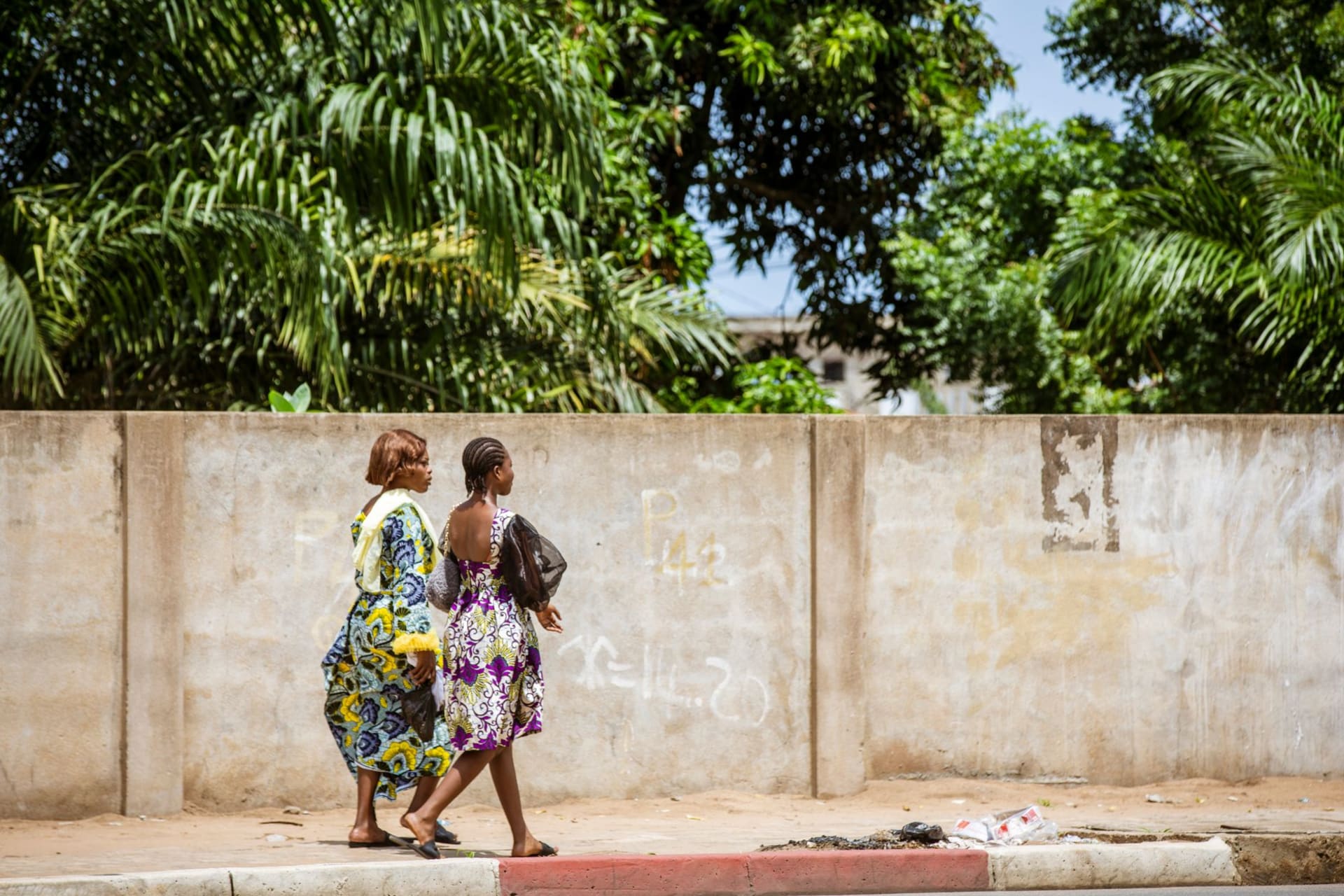 Two women in colorful African wax-print dresses walking along a busy street in Lomé, Togo