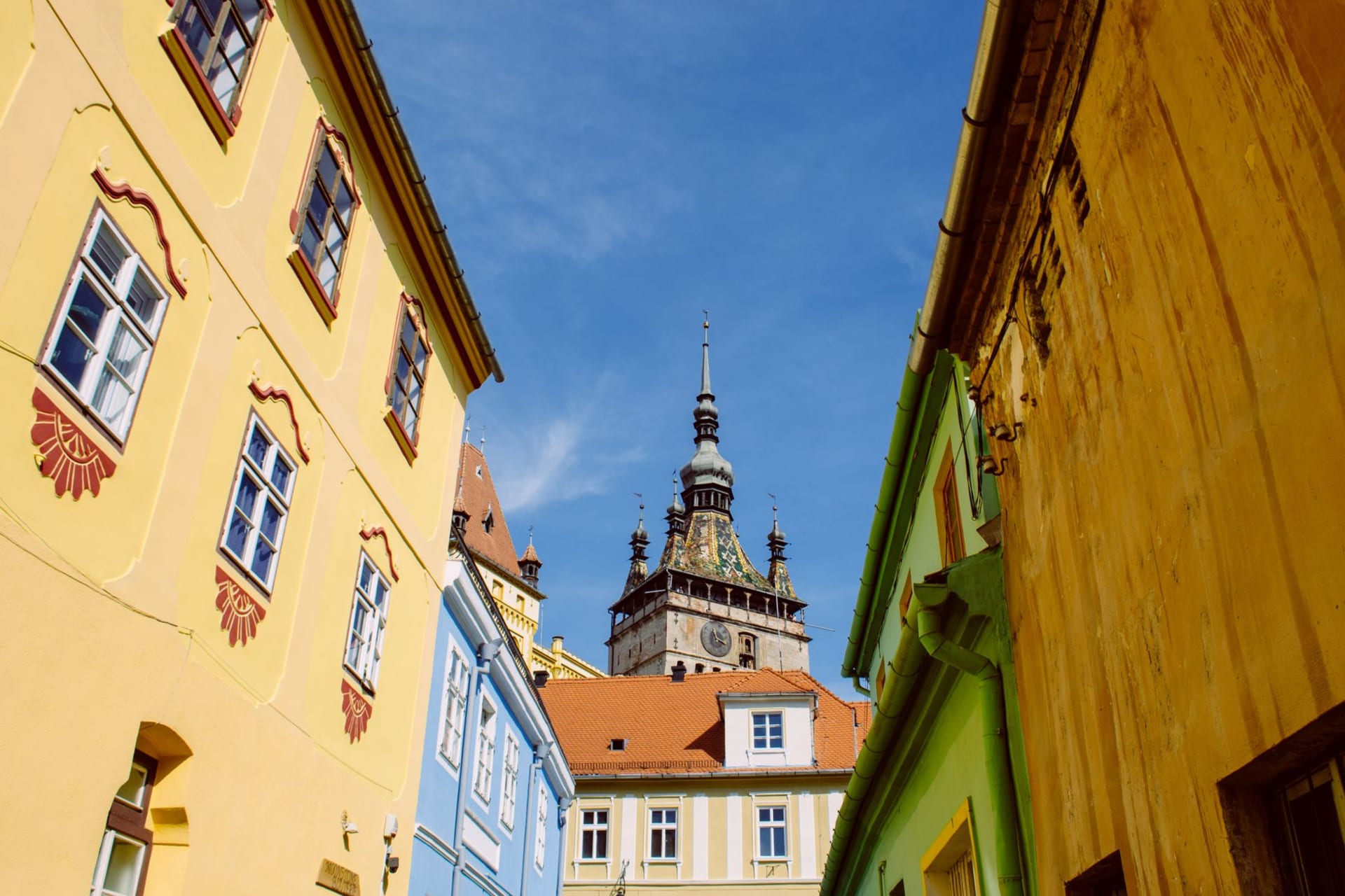 Sighisoara's Clock Tower rising above terracotta and ochre rooftops, with the forested citadel hill behind and a cloudy Transylvanian sky above