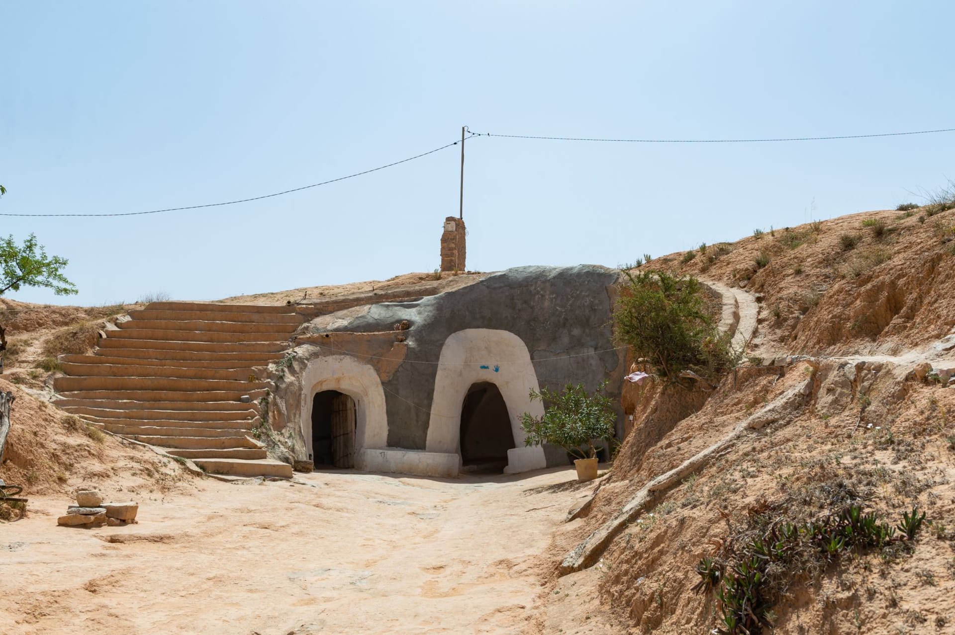 Vue prise depuis l'intérieur d'une habitation troglodyte traditionnelle de Matmata, l'ouverture circulaire vers le ciel encadrant un cercle parfait de bleu vif au-dessus des parois de terre ocre creusées et des portes taillées de la cour souterraine