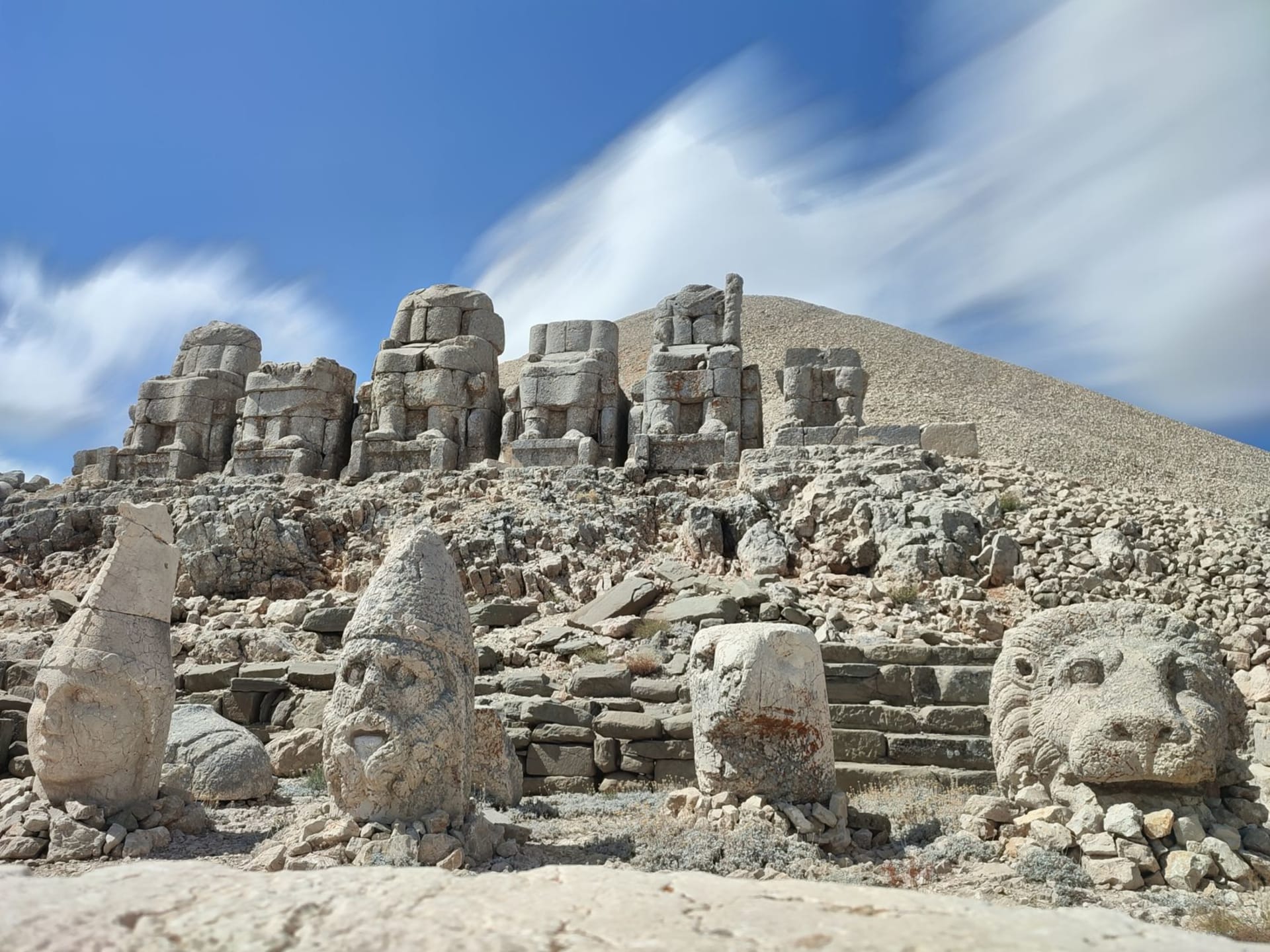 Colossal stone heads of ancient gods and kings on the summit of Mount Nemrut at sunrise, warm orange light catching their worn limestone faces against a vast Anatolian sky
