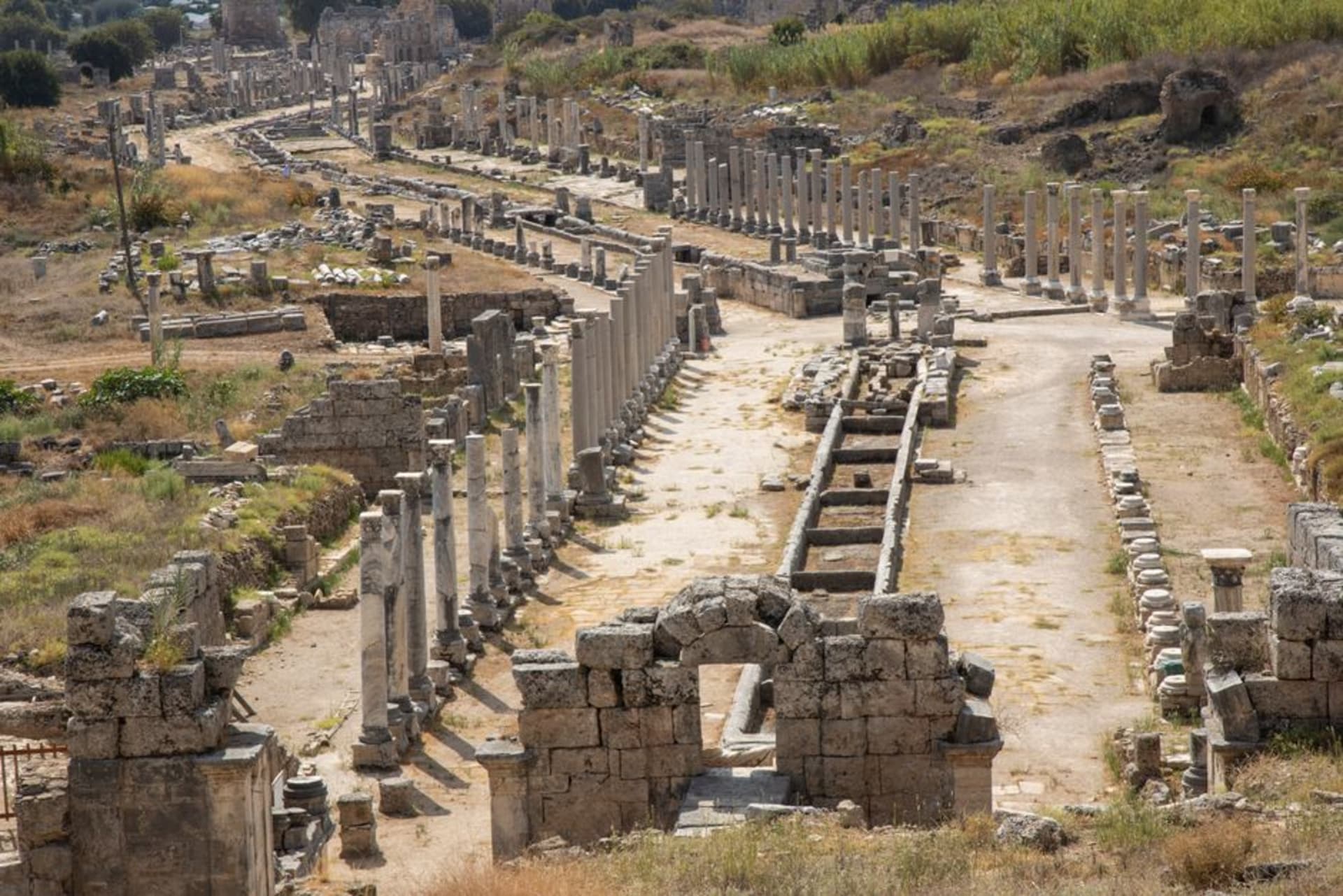 La rue principale à colonnades de l'antique Perge bordée de colonnes effondrées menant vers les tours de la porte hellénistique de la ville