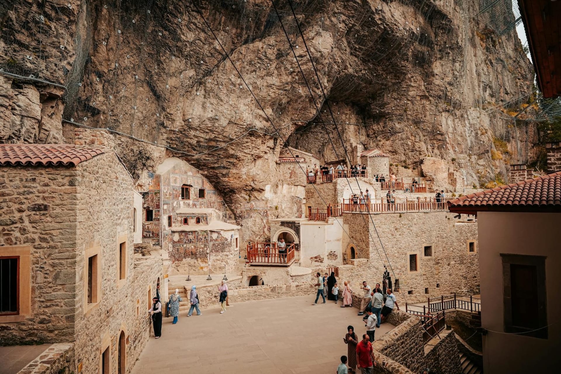 Sumela Monastery carved into a vertical limestone cliff face in the Pontic Mountains, its whitewashed facade and colonnaded galleries rising above a dense canopy of beech and pine forest in the Altındere valley.