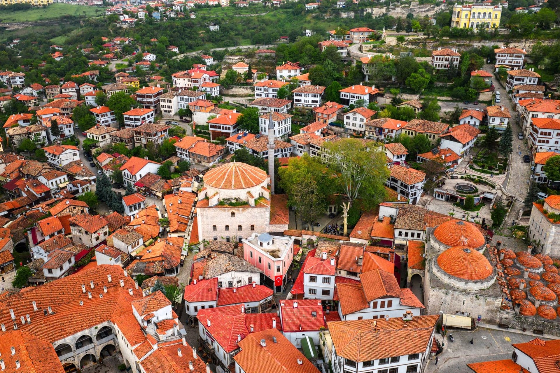 Rows of whitewashed Ottoman timber-framed houses with dark wooden beams climbing a steep hillside in Safranbolu's old quarter, under a grey-blue afternoon sky