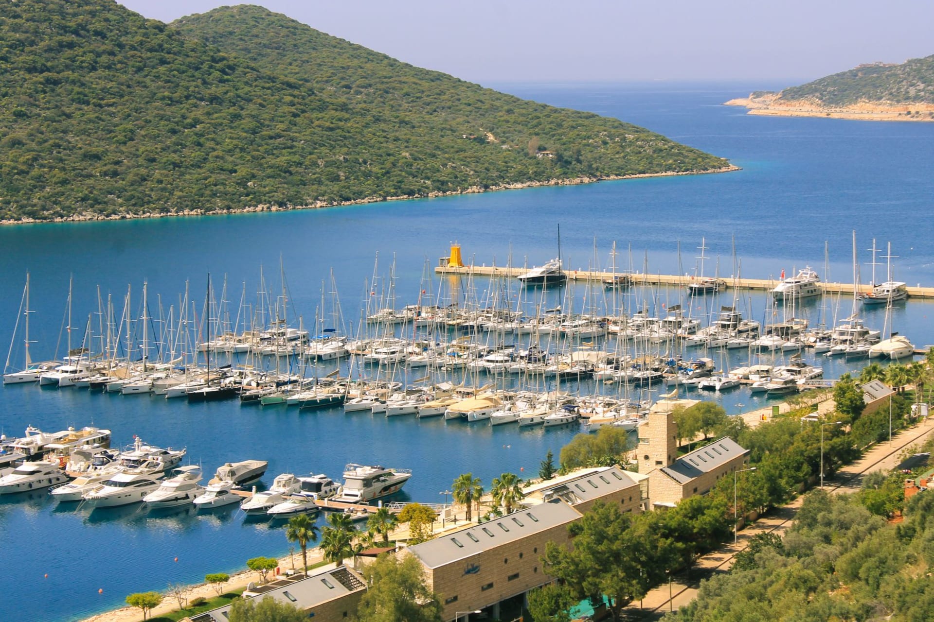The harbor of Kaş at sunrise, wooden gulets moored below limestone cliffs spilling with pink bougainvillea