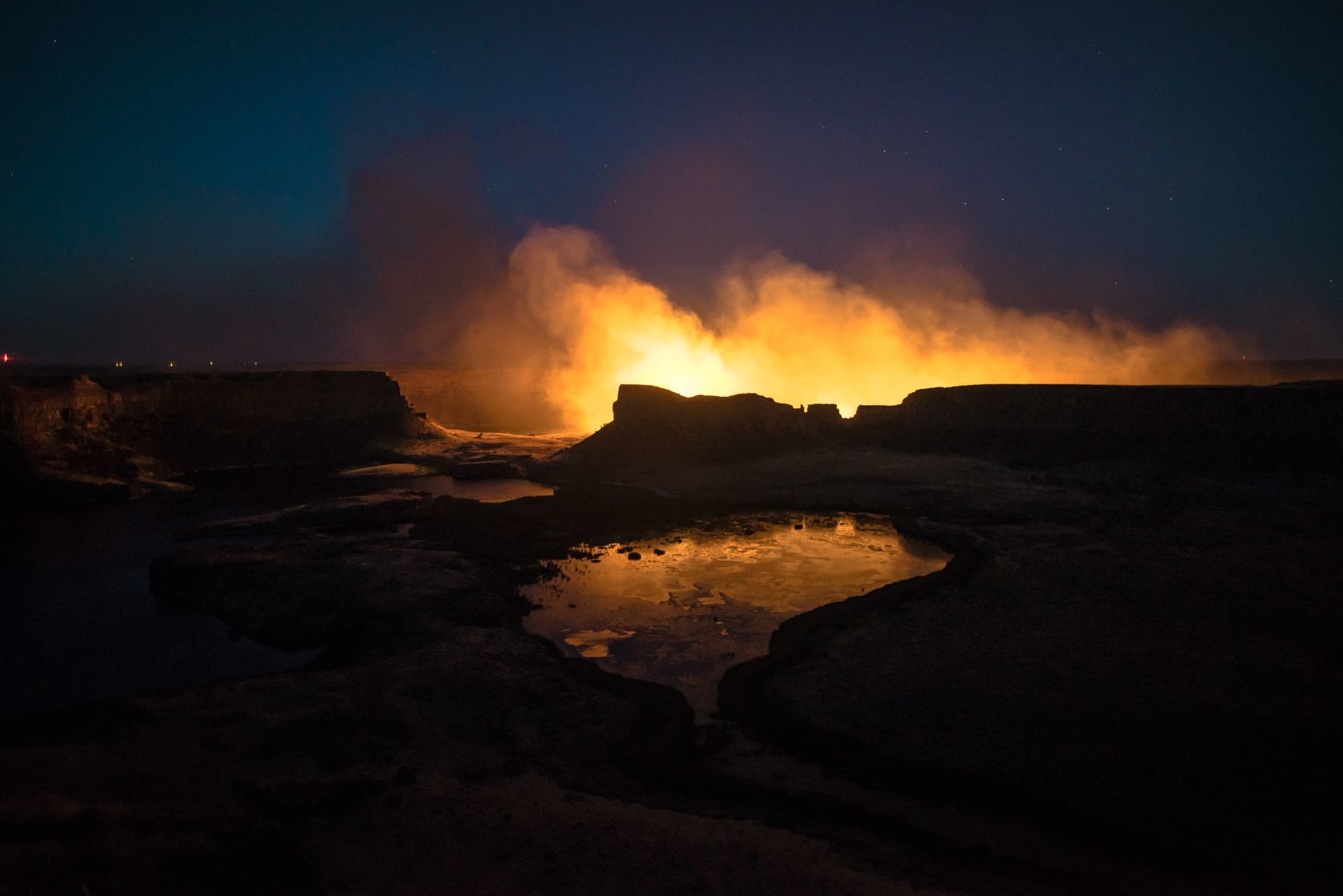 The Darvaza gas crater glowing orange in the darkness of the Turkmen desert, flames reflecting on the surrounding sand