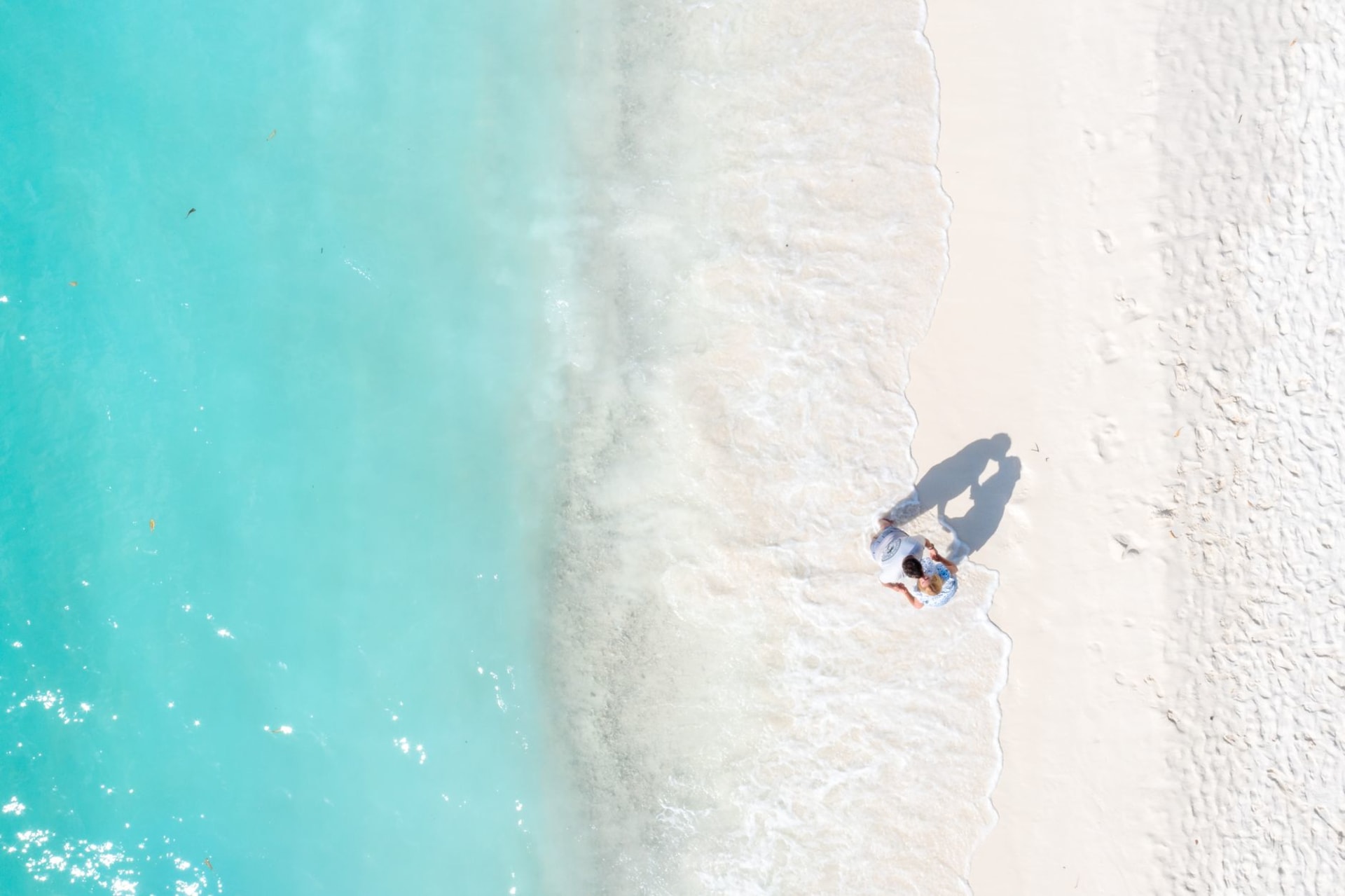 An empty white sand beach on Pine Cay stretching to a point, with low scrub vegetation and brilliant turquoise water, no structures visible