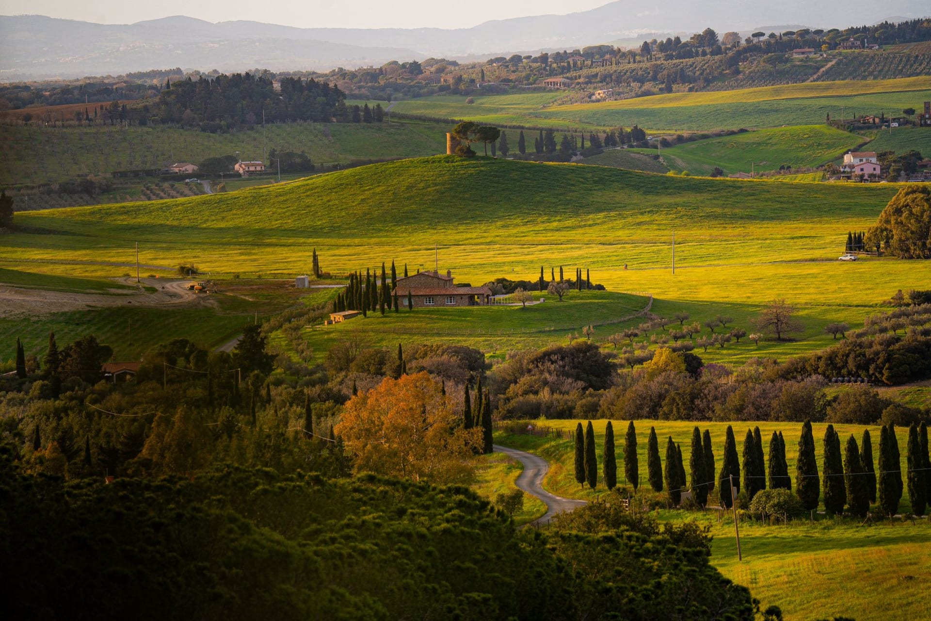 Aerial view of Tuscany's rolling hills layered in gold and green at sunset, with cypress lines cutting through the valley