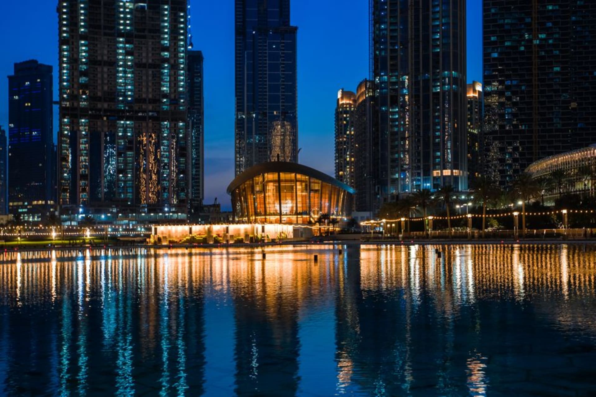 Dubai Opera's dhow-shaped building illuminated at night with the Burj Khalifa behind it