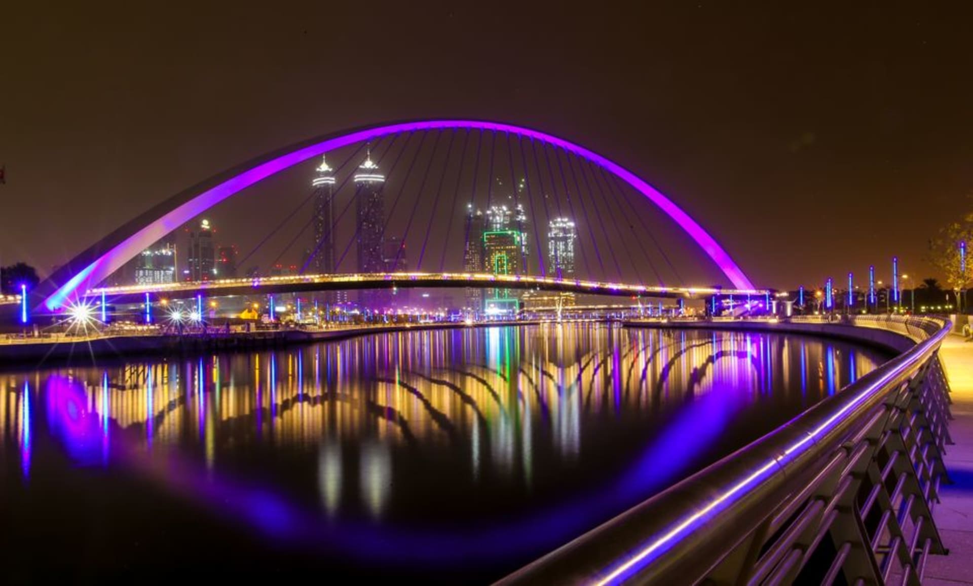 Canal de Agua de Dubái al atardecer con puentes iluminados y torres frente al agua reflejadas en ella