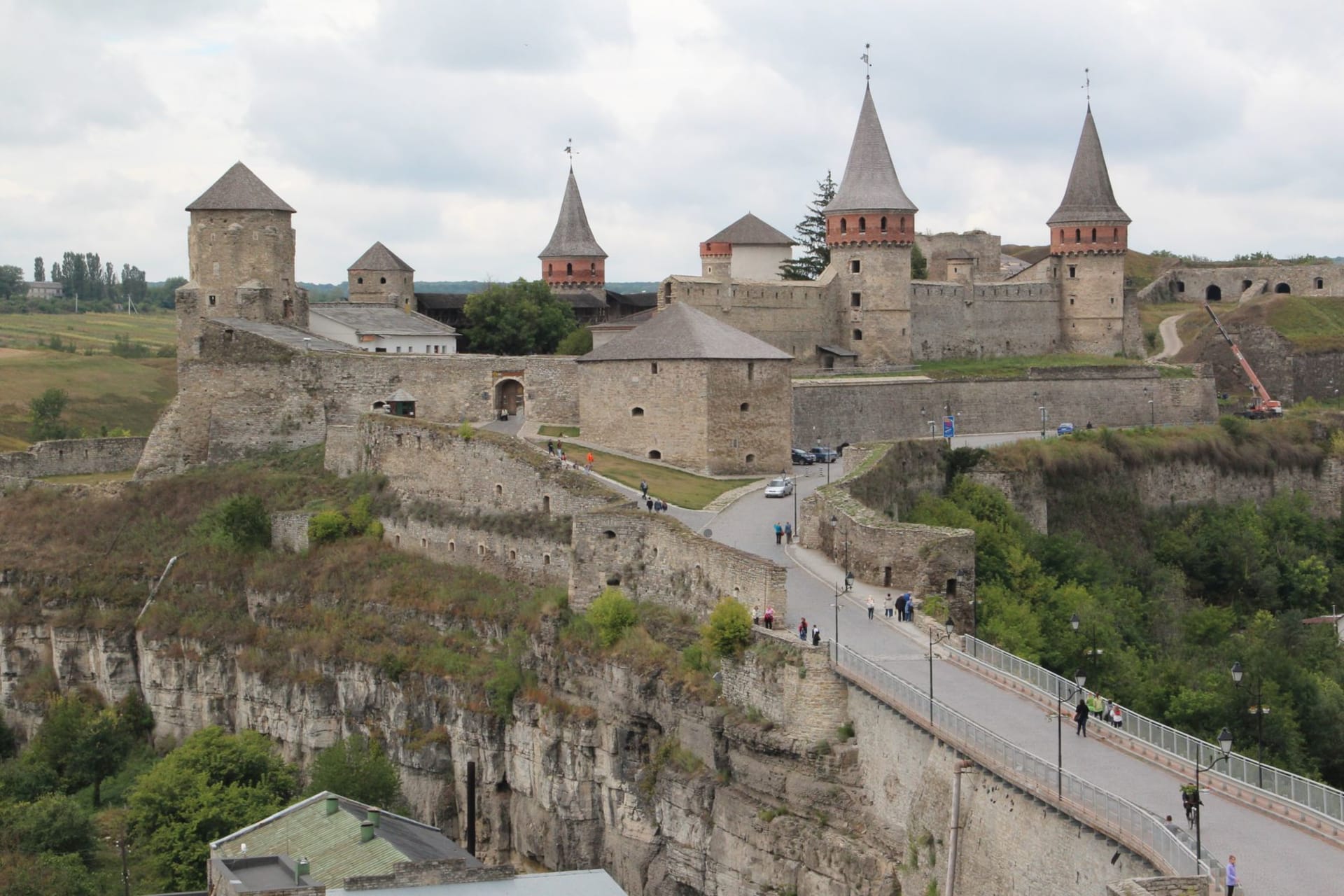 Kamianets-Podilskyi fortress rising from the canyon rim at dusk, its eleven towers reflected in the dark curve of the Smotrych River below