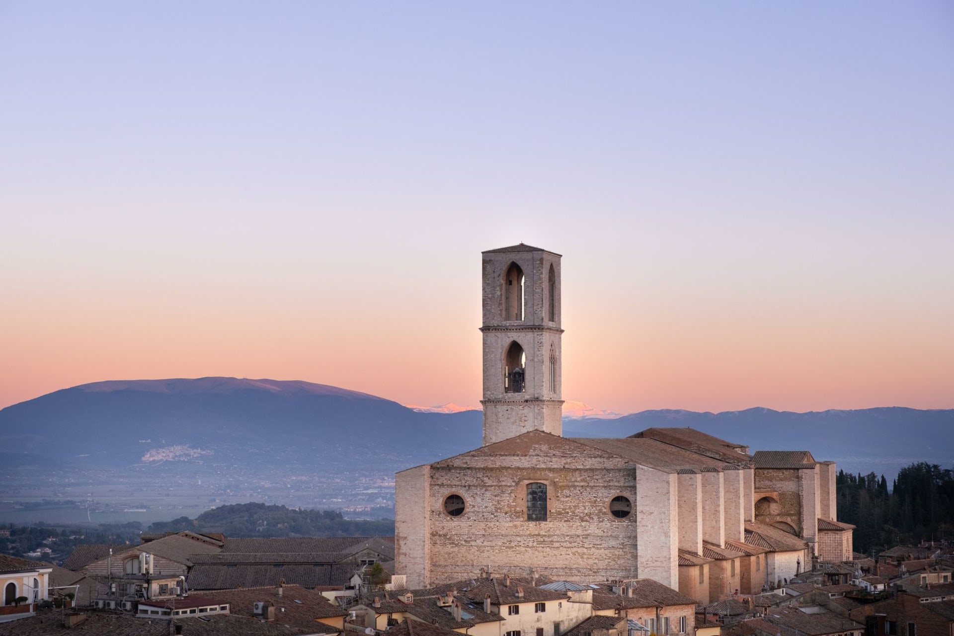 Le Palazzo dei Consoli en pierre grise de Gubbio s'élevant au-dessus des toits en terre cuite, le versant apennin se pressant de près derrière la ville médiévale compacte